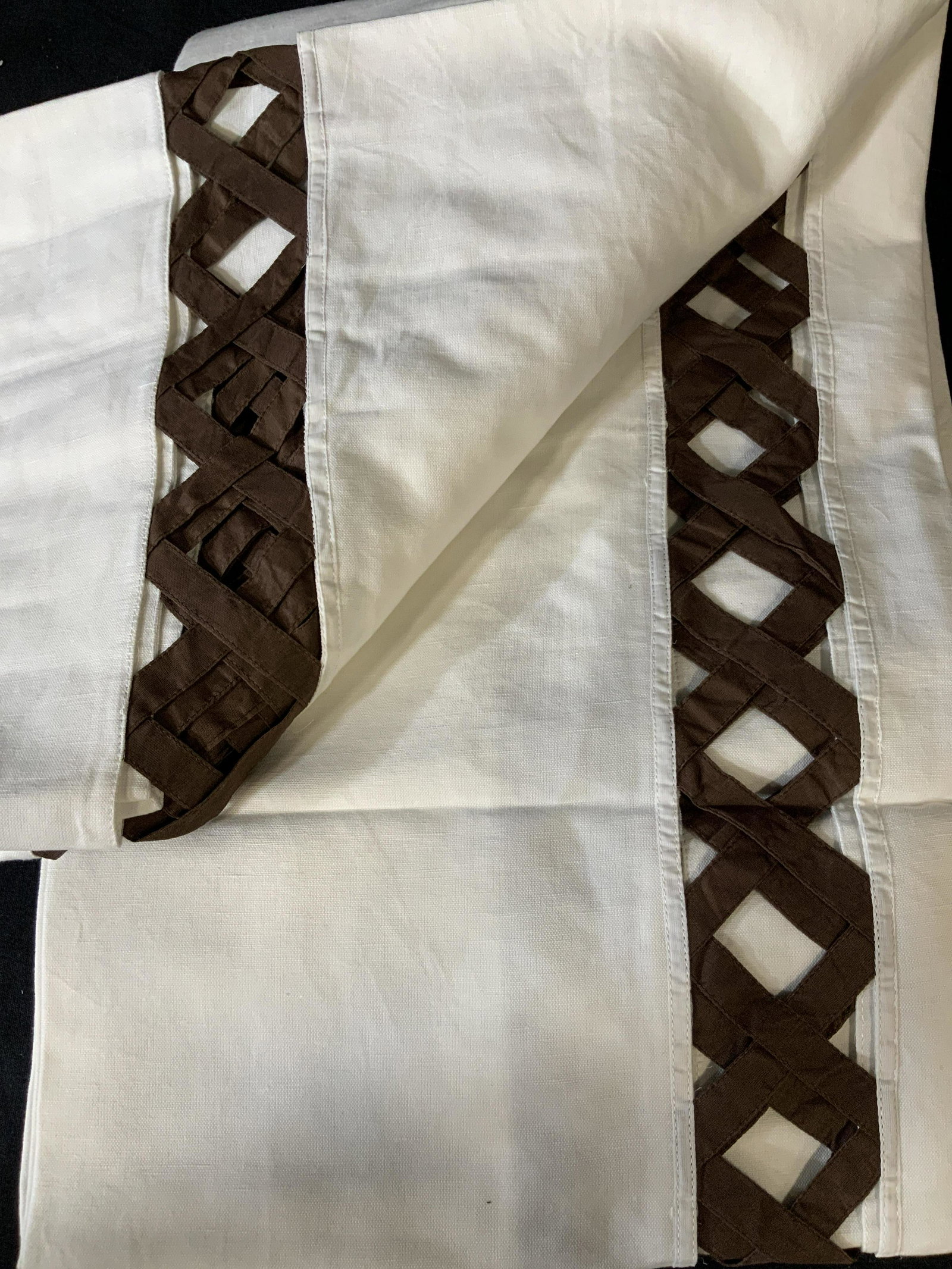 Set of Two Decorative Tablecloths: Set of two large table clothes in white with a brown peek-a-boo basket pattern around the edge of the table where it hangs over the side of the table, made of linen the basket pattern is in a coffee, 