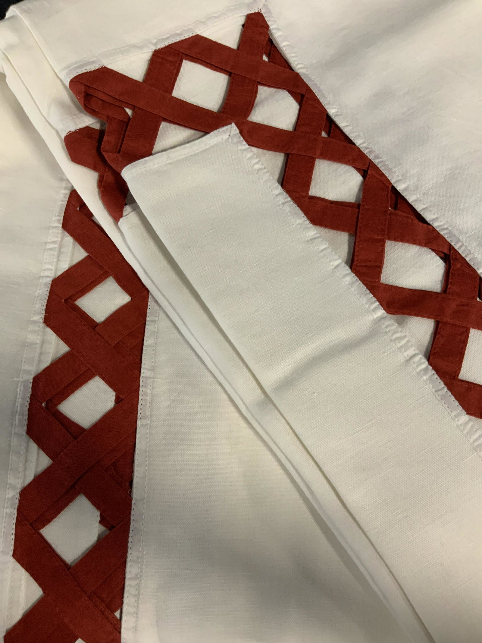 Set of Two Decorative Tablecloths: Set of two large table clothes in white with a red peek-a-boo basket pattern around the edge of the table where it hangs over the side of the table, made of linen the basket pattern is in a chili red,