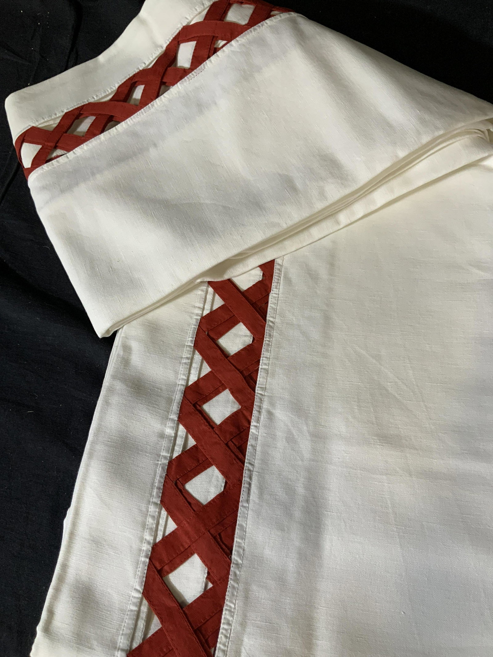 Set Of Two Decorative Tablecloths: Set of two large table clothes in white with a red peek-a-boo basket pattern around the edge of the table where it hangs over the side of the table, made of linen the basket pattern is in a chili red,