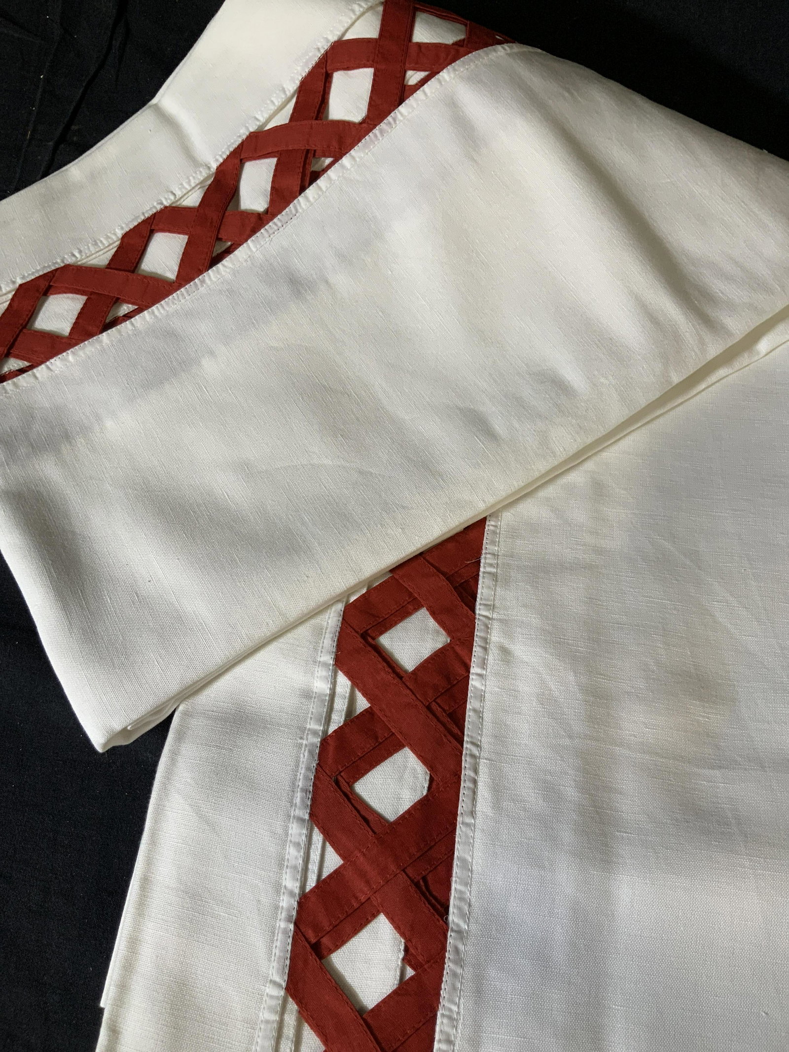 Set of Two Decorative Tablecloths: Set of two large table clothes in white with a red peek-a-boo basket pattern around the edge of the table where it hangs over the side of the table, made of linen the basket pattern is in a chili red,