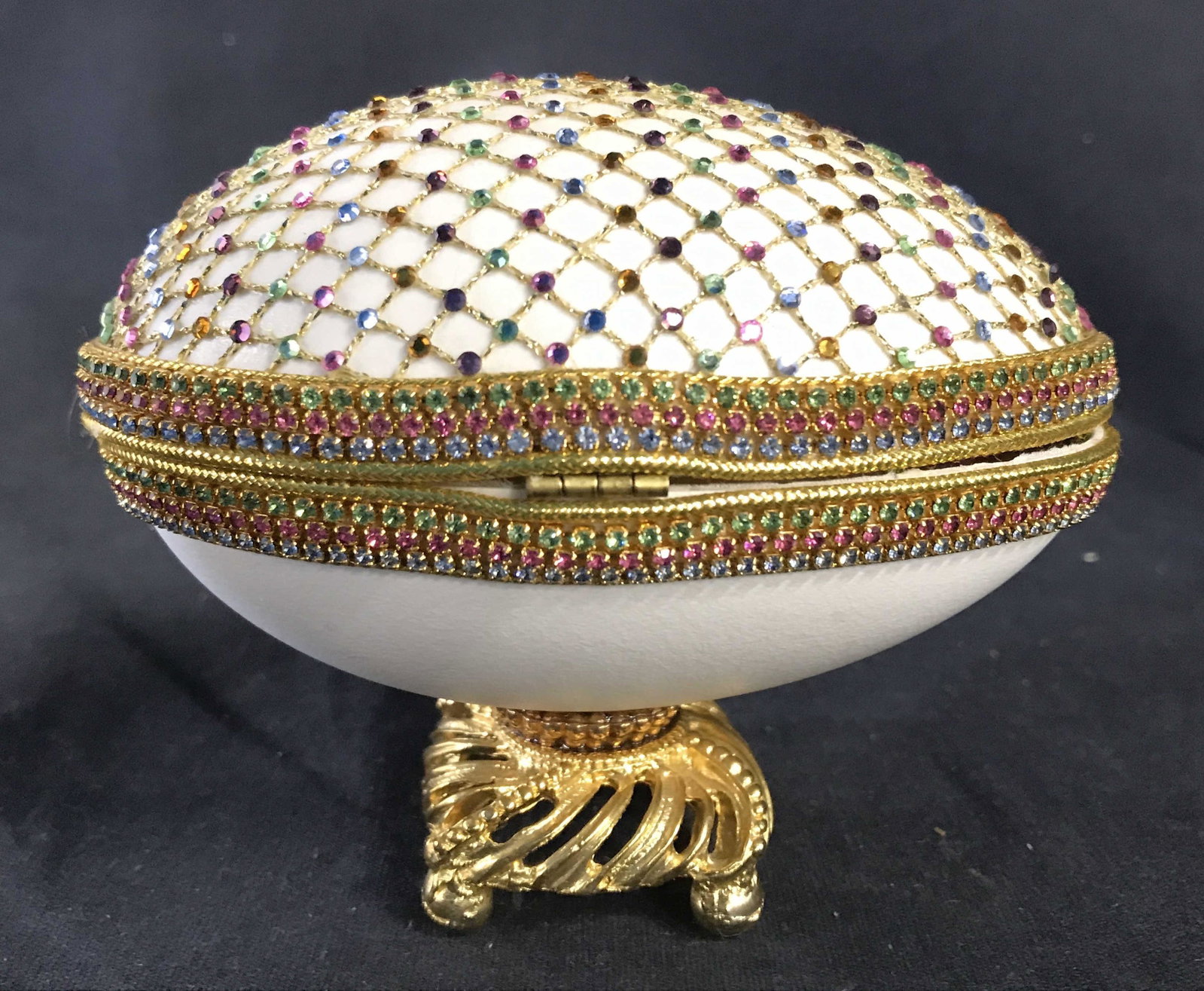 Pedestaled Faberge Egg Style Trinket Box: Trinket box resembles pedestaled Faberge egg. Piece has multiple tones of rhinestones and gold toned netting detail. Piece is attached to gold toned pedestal. Interior contains multi toned floral & le