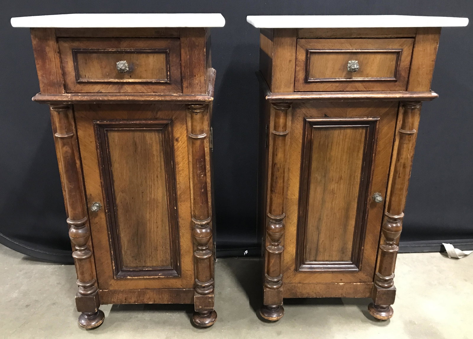 Vintage Marble Top Carved Wooden Side Tables: Side tables each have white toned marble tops. Pieces appear to have hand dovetailing. Each have 1 drawer and 1 cabinet door. Interior of cabinet doors have 1 shelf. Drawers have petite gold toned kno