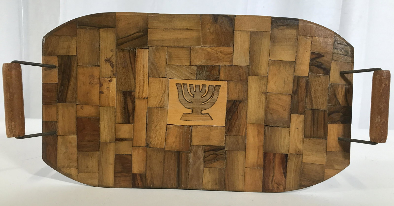 Vintage Wooden Judaica Tray W Handles: Tray is wooden. Piece has image of a menorah in center. Piece appears to made from inlaid sections of wood. Handles are wooden and metal. Piece measures approximately 14 inches long 7 inches deep. App