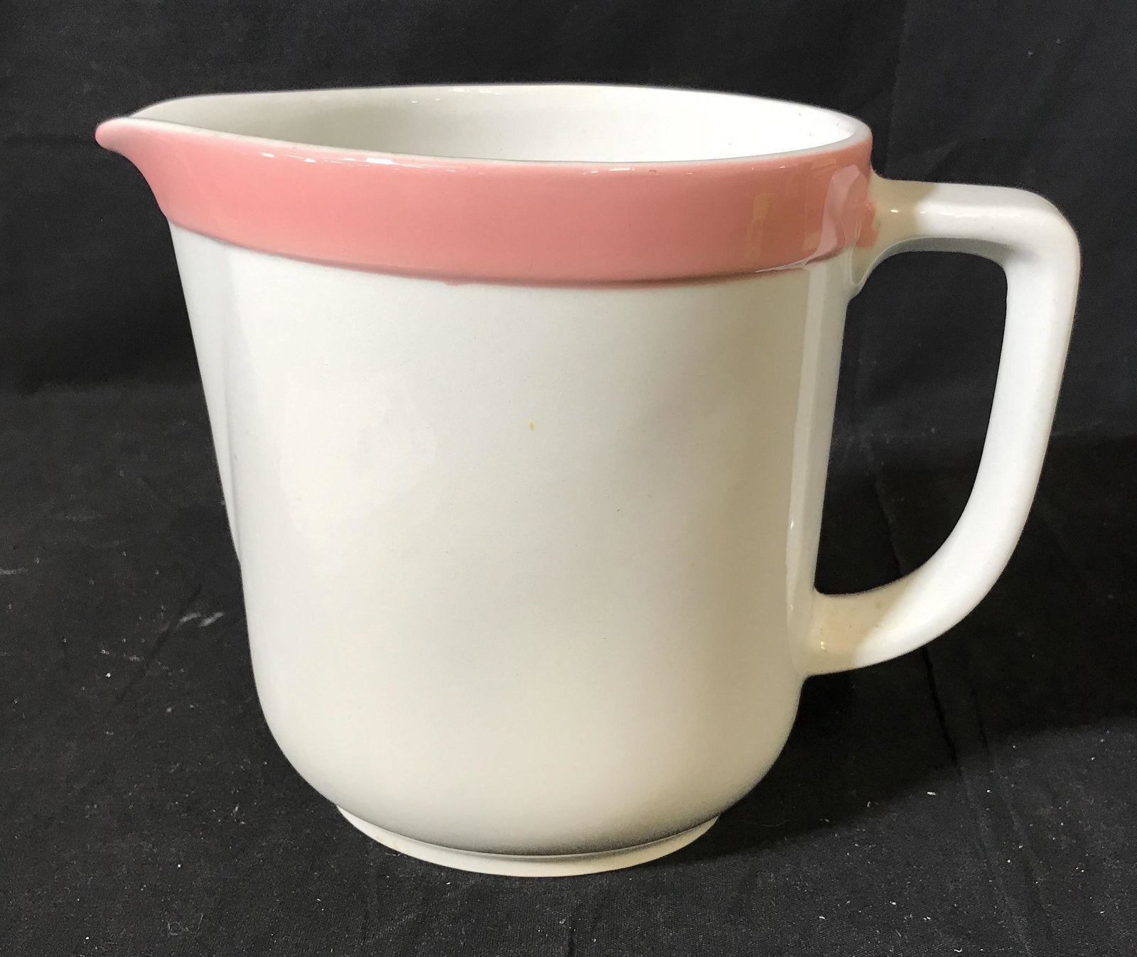 Arabia Made in Finland Porcelain Pitcher: Arabia made in Finland porcelain pitcher, stamp to bottom reads ‘Arabia Made in Finland 10’ with a crown above it, pitcher is white with a painted pink rim, measures 7.75 inches tall and 9.5 inche