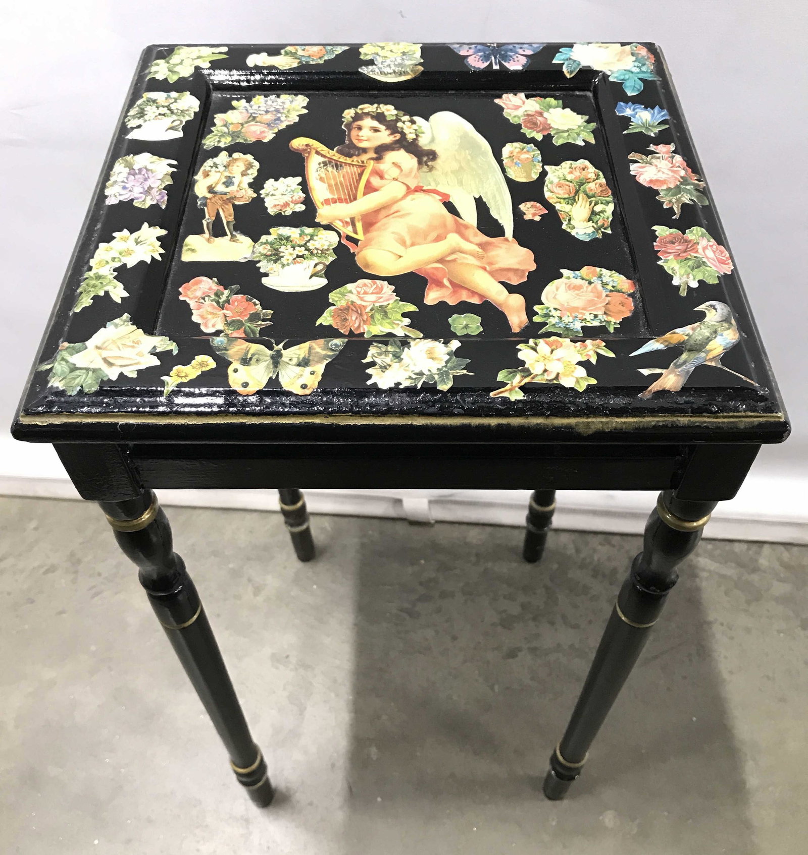 Vintage Lacquer Floral Cherub Detailed Side Table: Side table is black toned and lacquered. Piece has Multi toned floral, leaf and cherub detail. Piece appears To be wooden. Piece measures approximately 21 inches tall 12 inches square. Side table, end