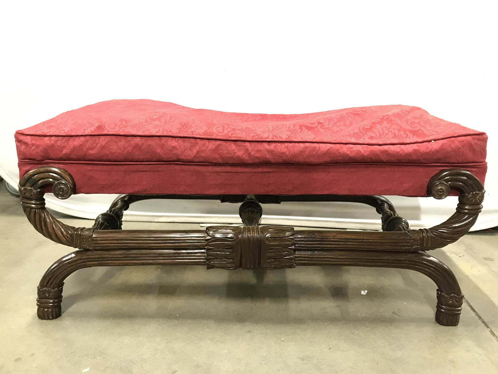Vintage Carved Wooden Bench W Upholstered Seat: Bench has intricately carved wooden detail. Piece is vintage possibly antique. Piece also has carved wooden stretchers between legs. Piece has red toned upholstery with floral and leaf detail. Piece m