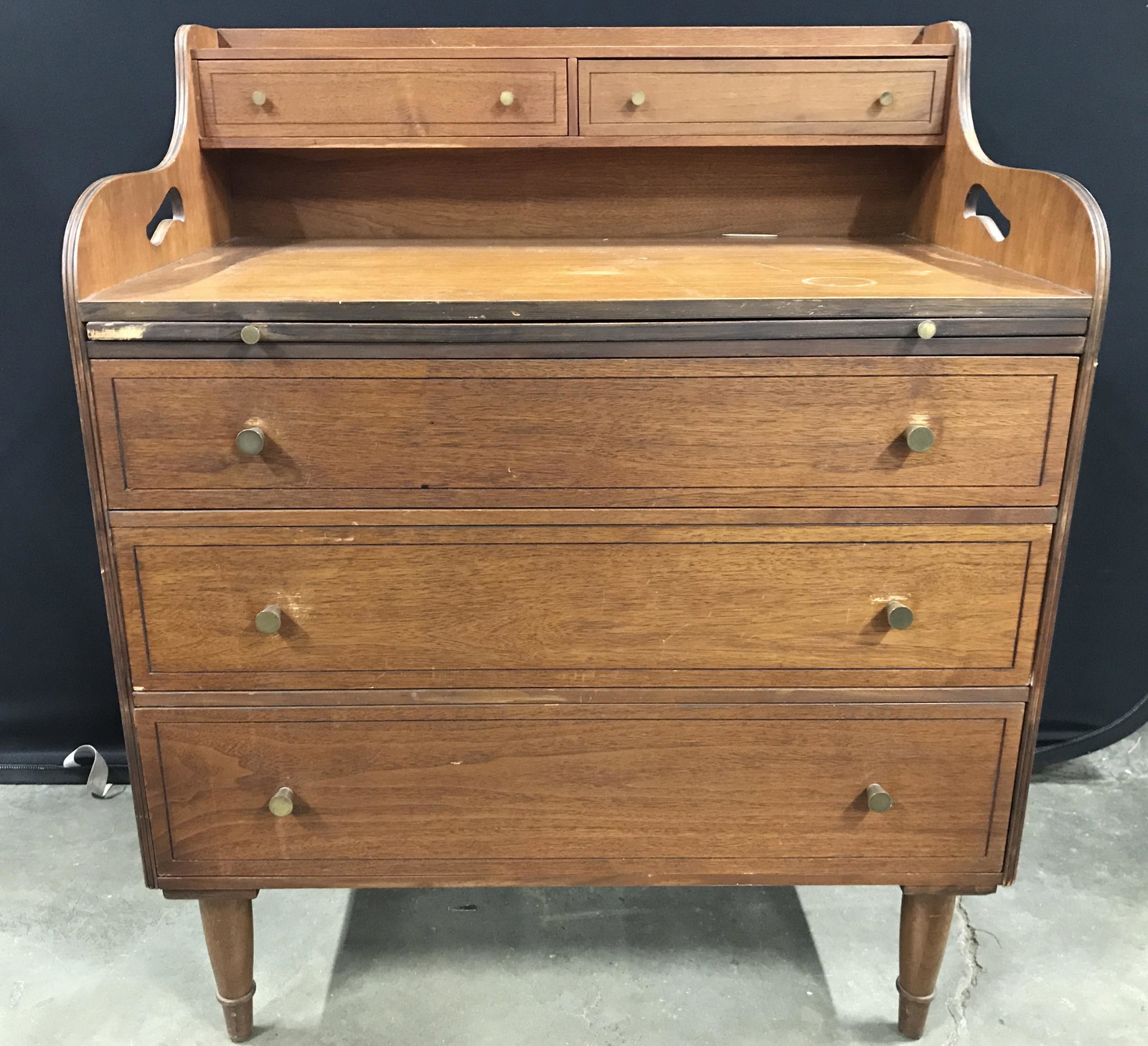 Vintage Carved Wooden Writers Desk: Writers desk is wooden. Piece is vintage possibly antique. Desk has brown toned leather pullout area. Top half has 2 petite size drawers lower half has 3 drawers each with gold toned knob style brass 