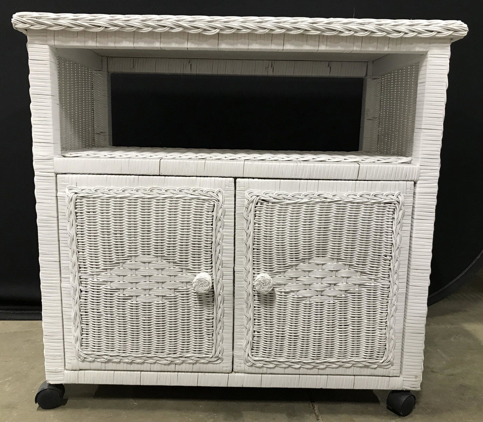 White Toned Woven Wicker Cabinet On Wheels: Cabinet is white toned and wicker. Piece has 2 cabinet doors which open up to storage area. Piece sits on 4 wheel. Cabinet doors have knob style handles. Piece measures approximately 29 inches tall & 