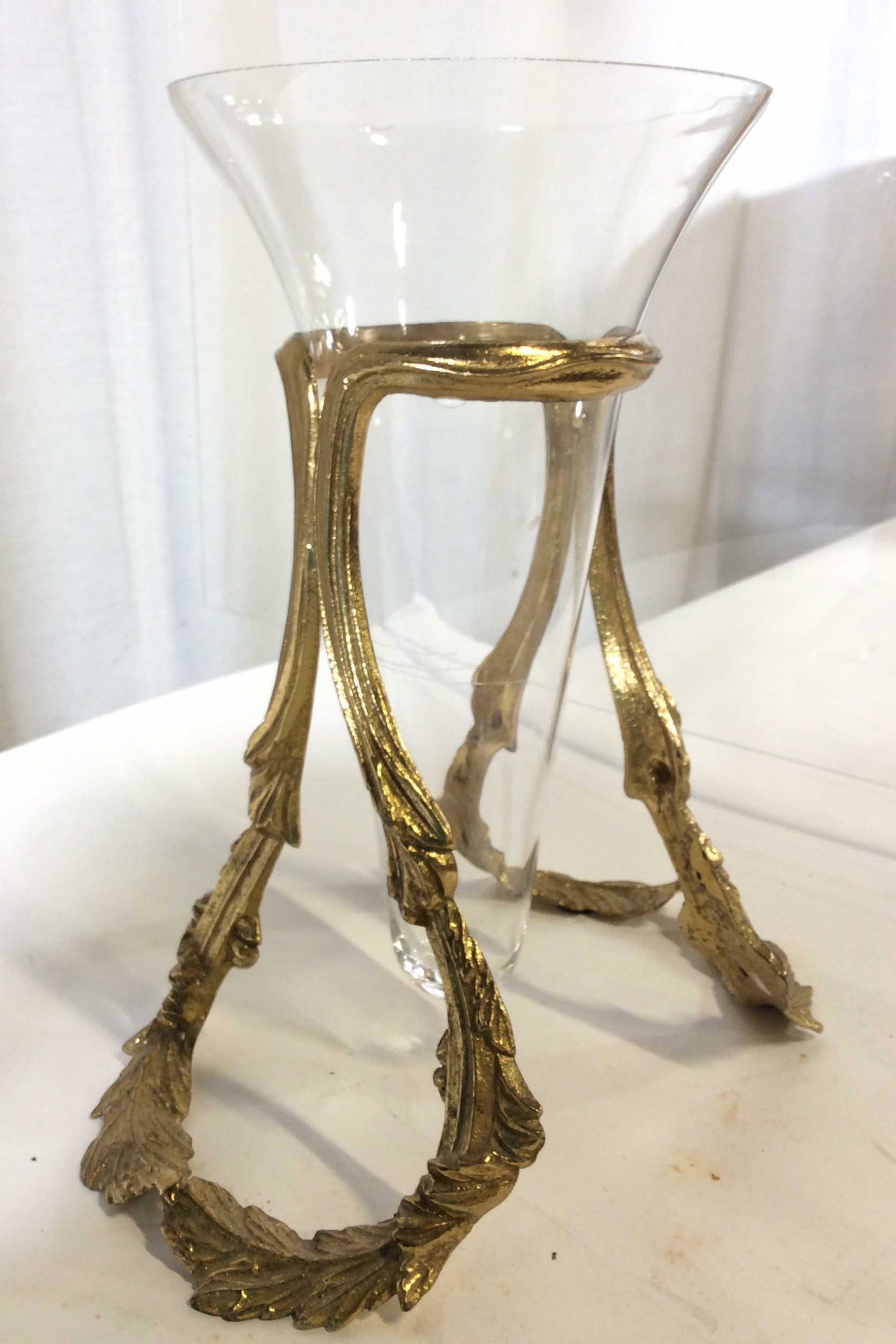 Glass trumpet vase set in Gold tone Stand: Embossed Roman laurel sides hold glass vase off of table in center. Rim to vase has chip, Gold toned base. 11 in ht. Base 6 1/4 in Width. Decorative Glass Vase in Stand, Gold Tone Roman Laurel Metal S