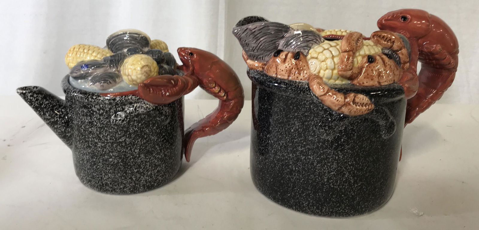 OMNIBUS FITZ AND FLOYD Pair Hand Painted Pitchers: Pair of crustacean themed pitchers, both have handles made to look like lobsters, both are decorated with clams corn and crabs, the smaller of the two has a lid, the larger has a label to the side tha