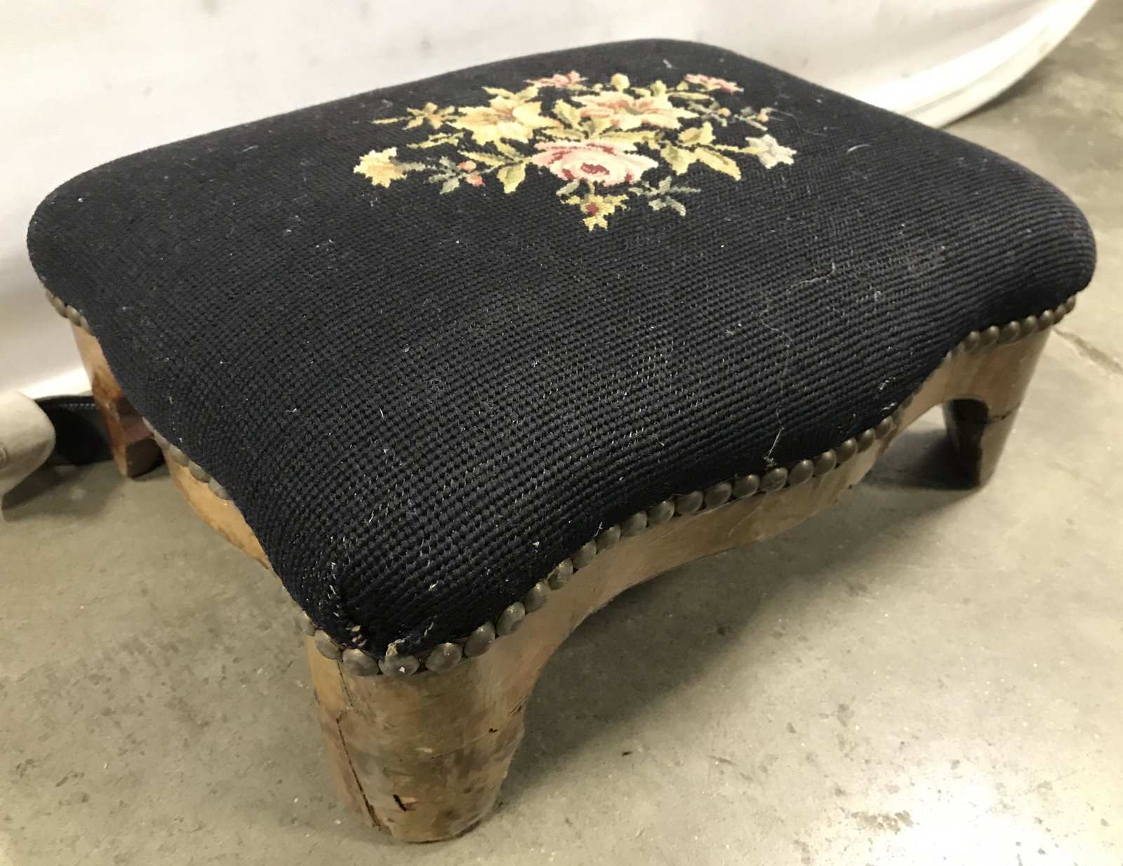 Antique Needlepoint Footstool: Footstool is upholstered with floral and leaf detail needlepoint / cross stitch upholstery. Piece has carved wooden feet. Edges of upholstery have nailhead detail. Piece measures approximately 14 inch