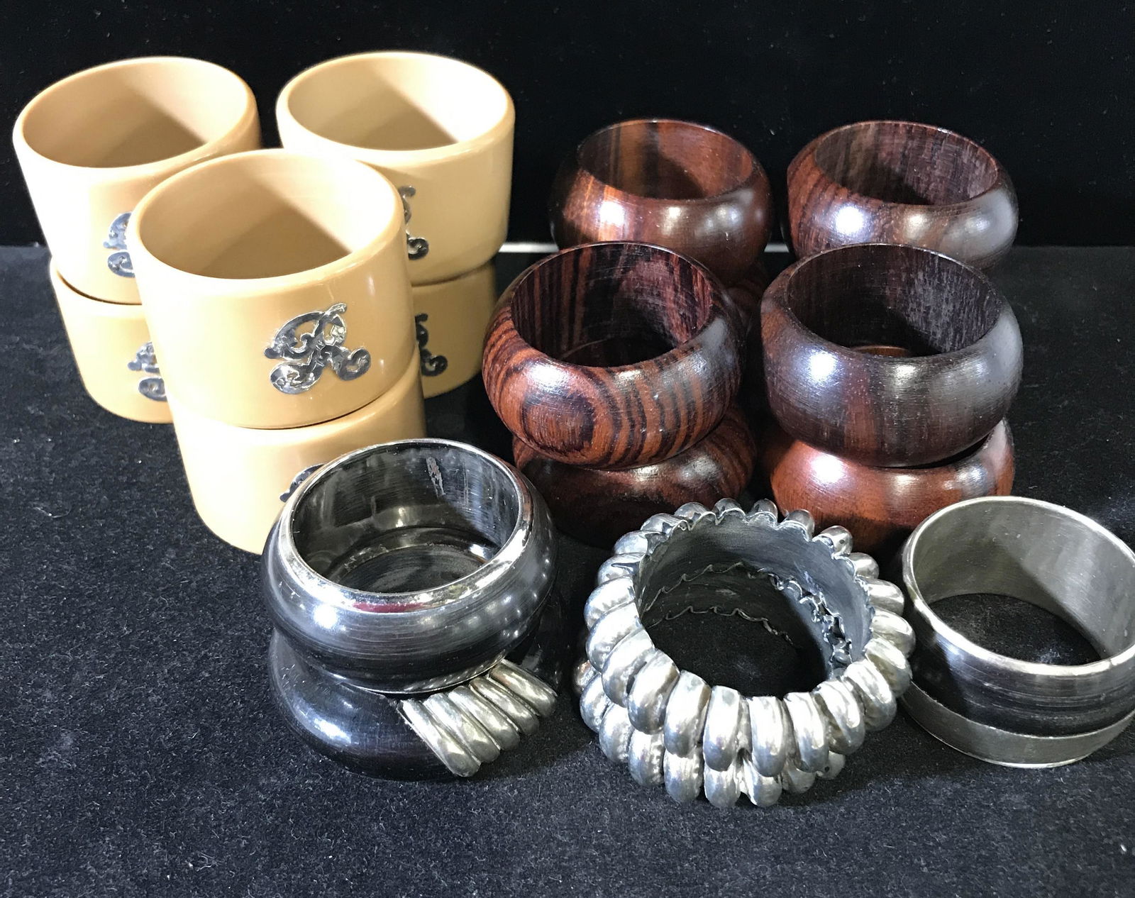 Lot 19 Napkin Rings: 19 rings, varying styles. Crafted from various materials, including wood, plastic, metal, and composite materials. Largest ring measures approx 1.75 inches H and 1.25 inches W. Wear is consistent with