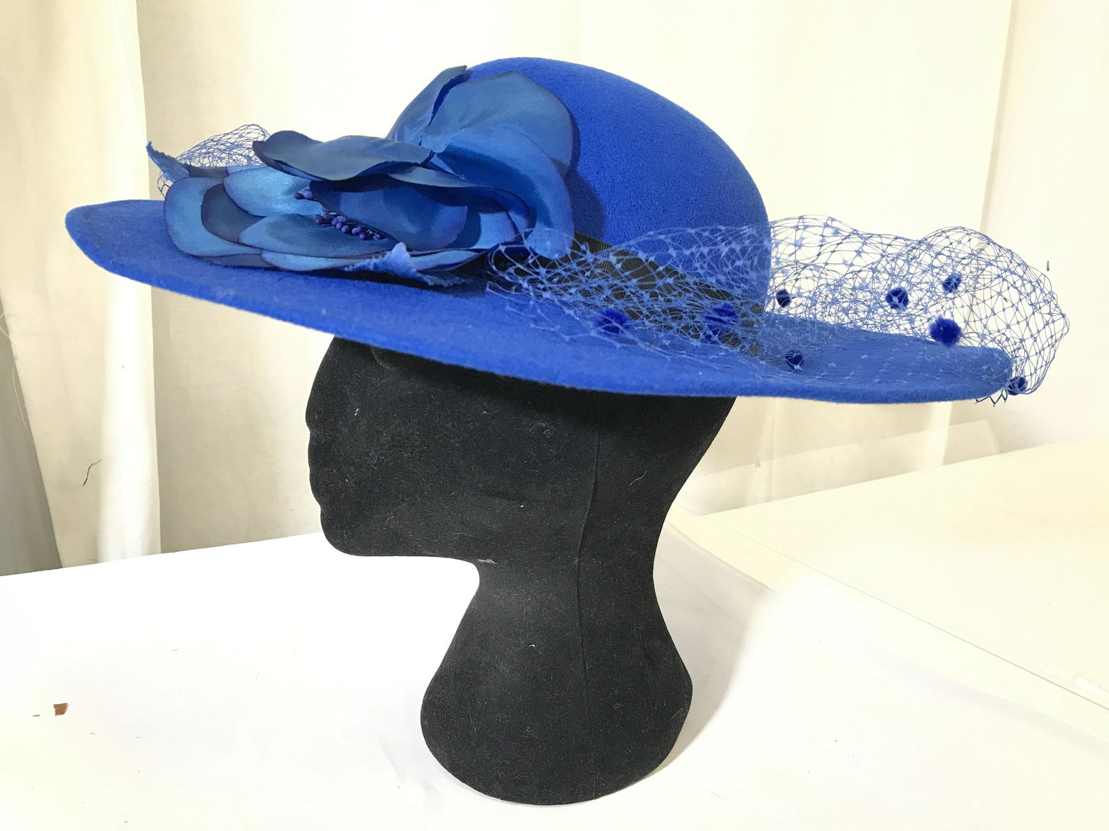 LIZ CLAIBORNE Blue Toned Women’s Hat: Interior has tag which reads LIZ CLAIBORNE. Piece is blue toned with black toned hat ribbon & blue netting. Piece also has blue toned floral style hat ornament. Hat, women’s hat, wearables, fashion