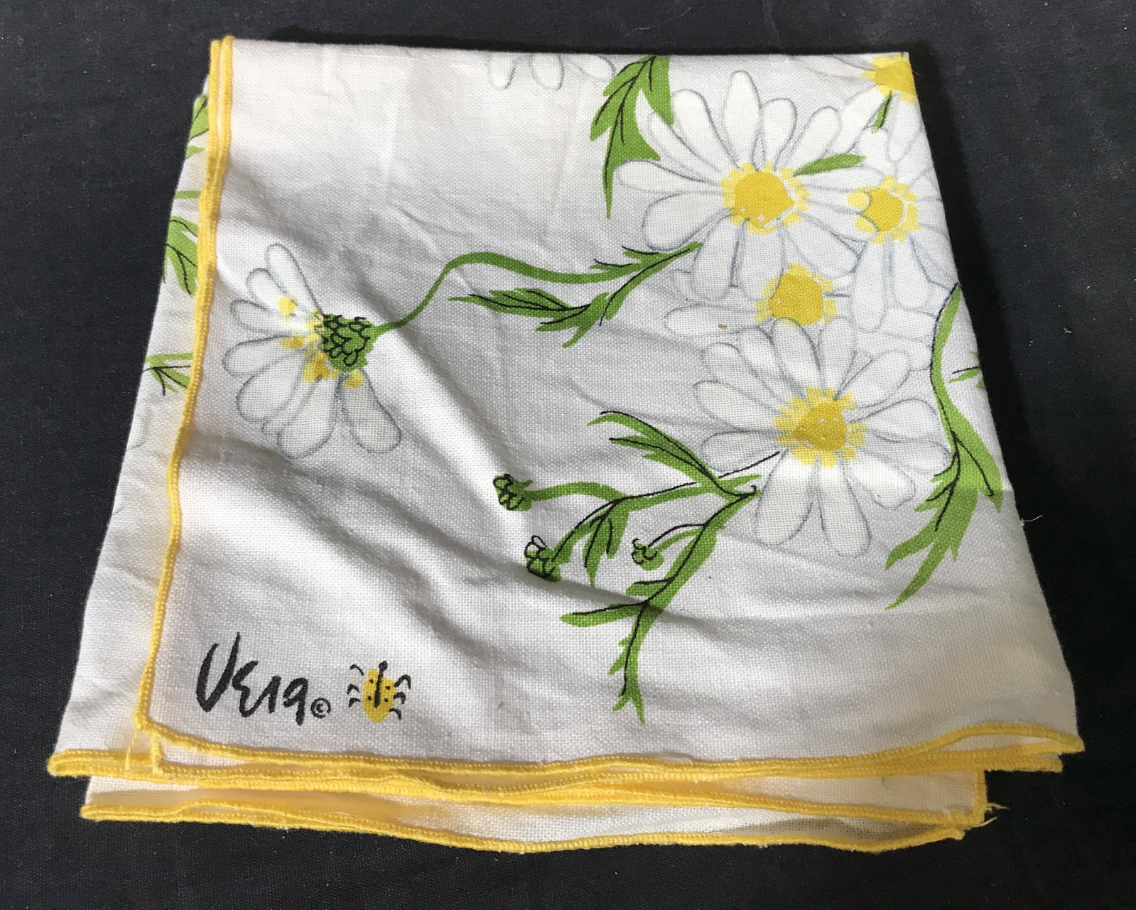 Group lot Yellow & Floral Linens: Group lot of 5 yellow and floral linens, lot includes four napkins two of which have daisy patterns to them with a logo that reads ‘Vera’ and a yellow table clothe, all linens have been cleaned st