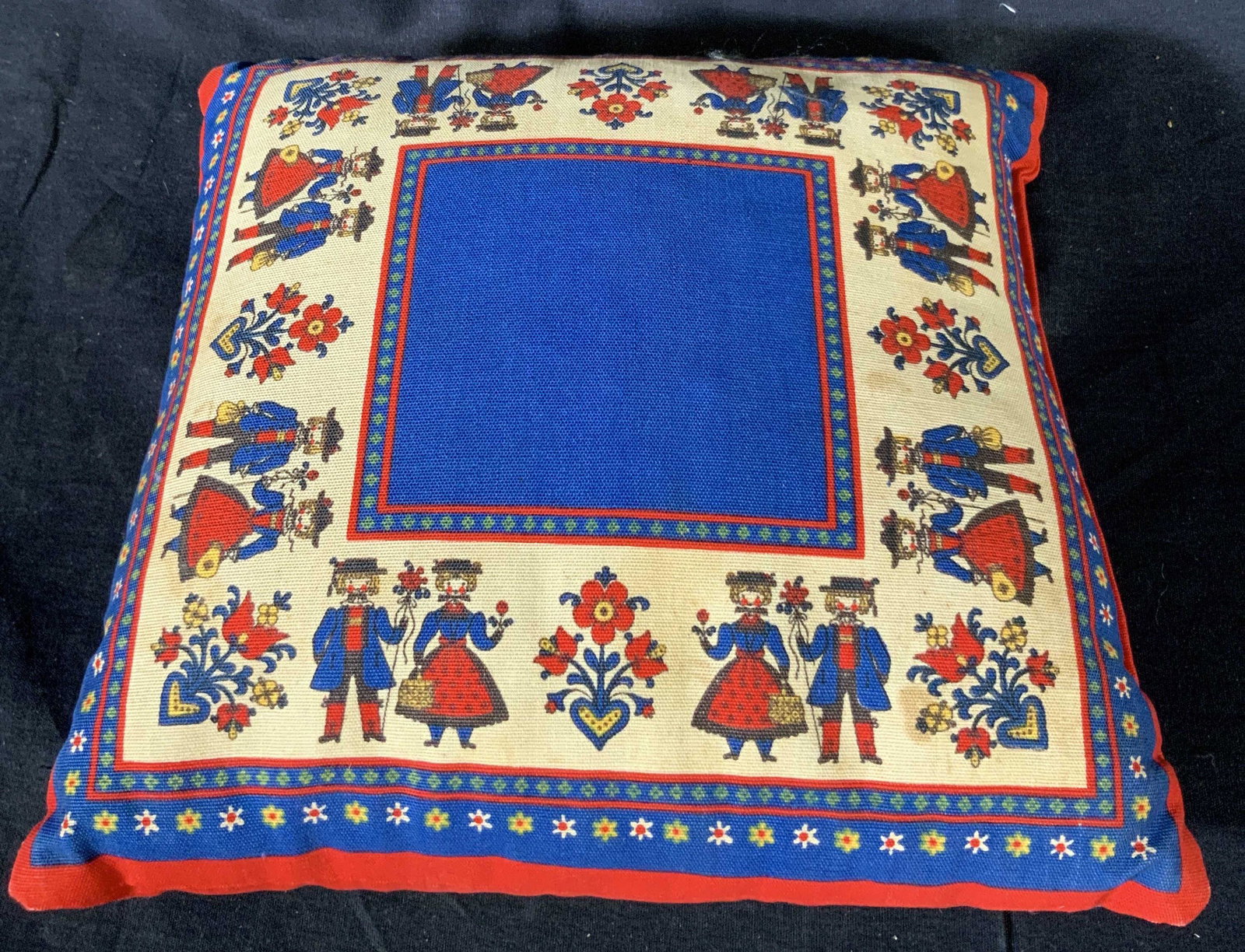 Decorative Folk Art Pillow: Small pillow with decorative fabric depicting sets of couples in classic Dutch or Scandinavian dancing clothes that is commonly seen in historical folklore, the main colors of the pillow are blue red 