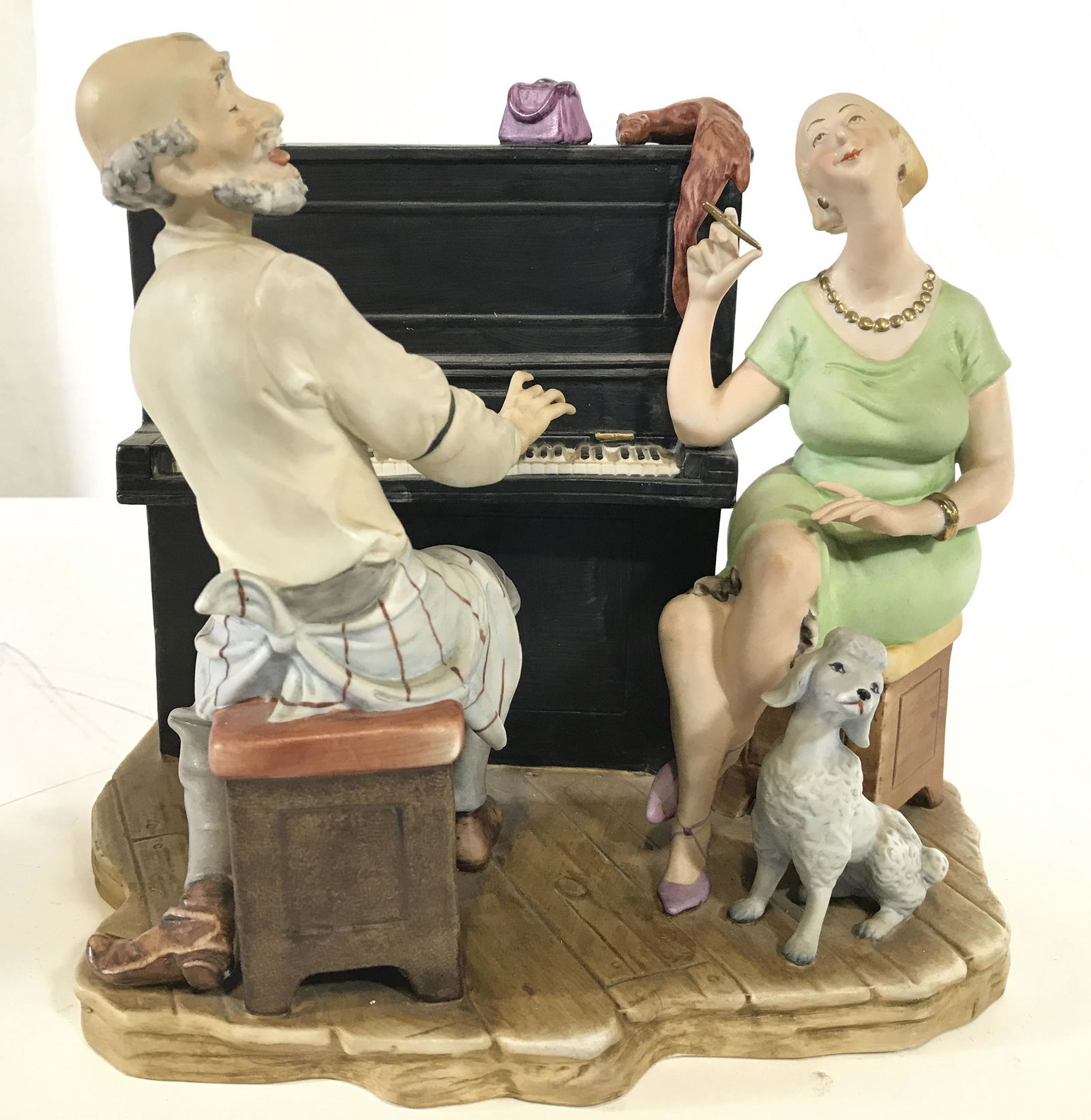 Vintage Porcelain Piano Player Music Box: Figural depicts a male figure playing piano next to a female Figure & dog figure. Piece appears to possibly be hand painted. Underside reads N. Possibly NIPPON. Piece measures approximately 8 inches t