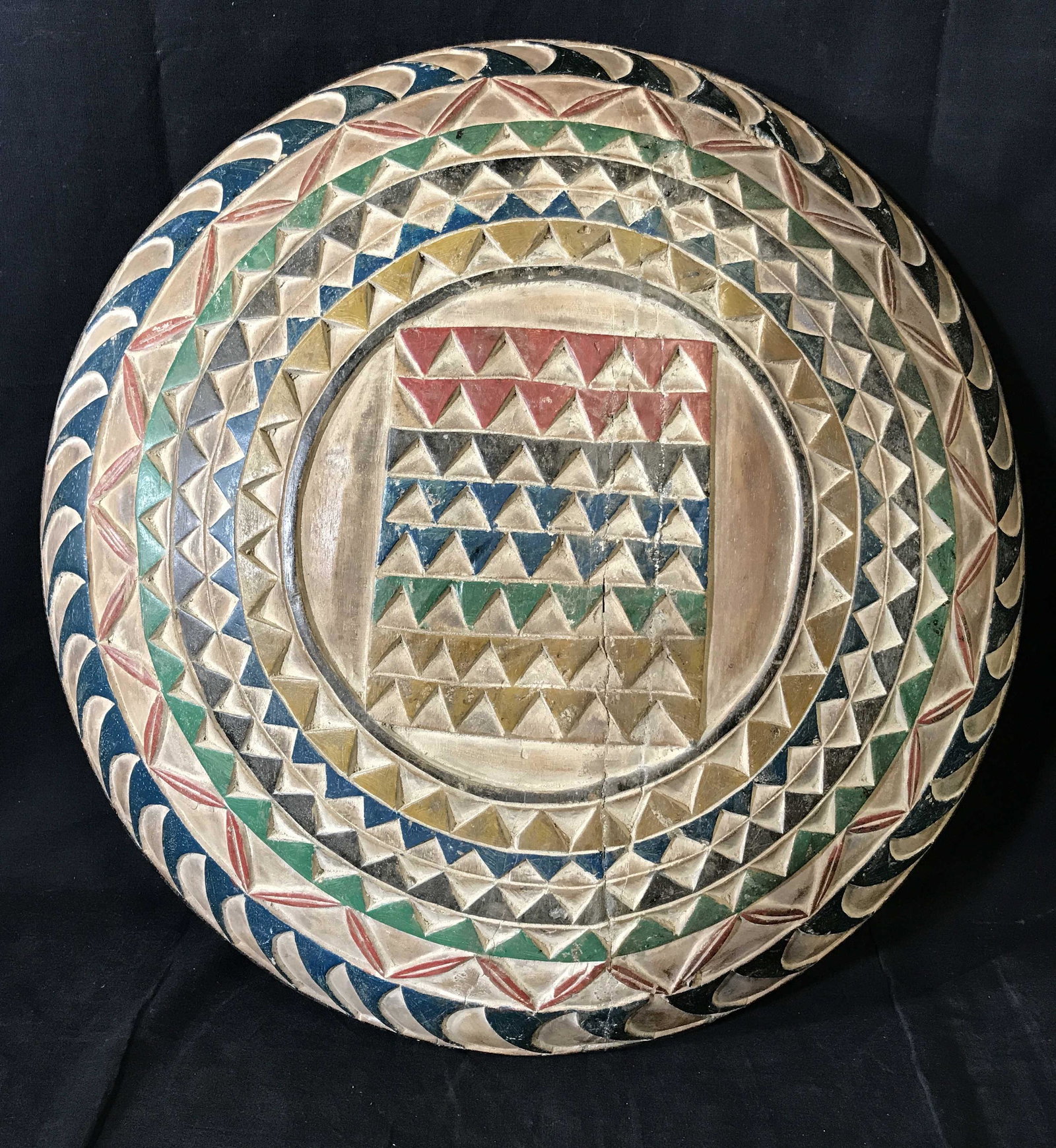 Ceremonial Zulu Shield: Ceremonial Zulu Shield, origins can be found in South Africa, wooden shield with colorful pigments in triangles and geometric designs to the surface, handle carved into the back, diameter approximatel