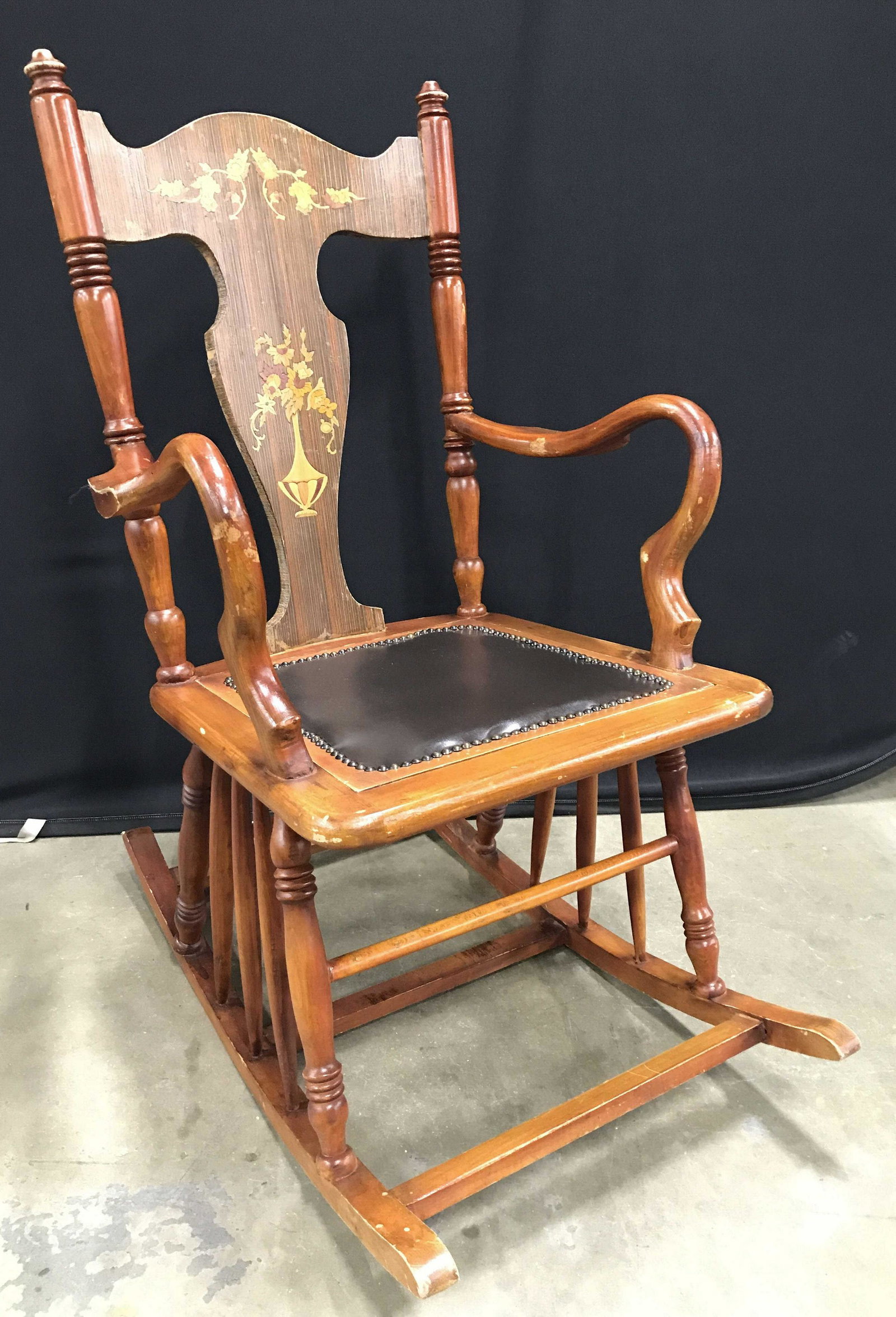 Vintage Wooden Rocking Chair W Leather Seat: Rocking chair Is vintage possibly antique. Chair has black toned upholstered seat which appears to possibly be genuine leather. Seat has nailhead detail around upholstery. Backrest has floral & vase d