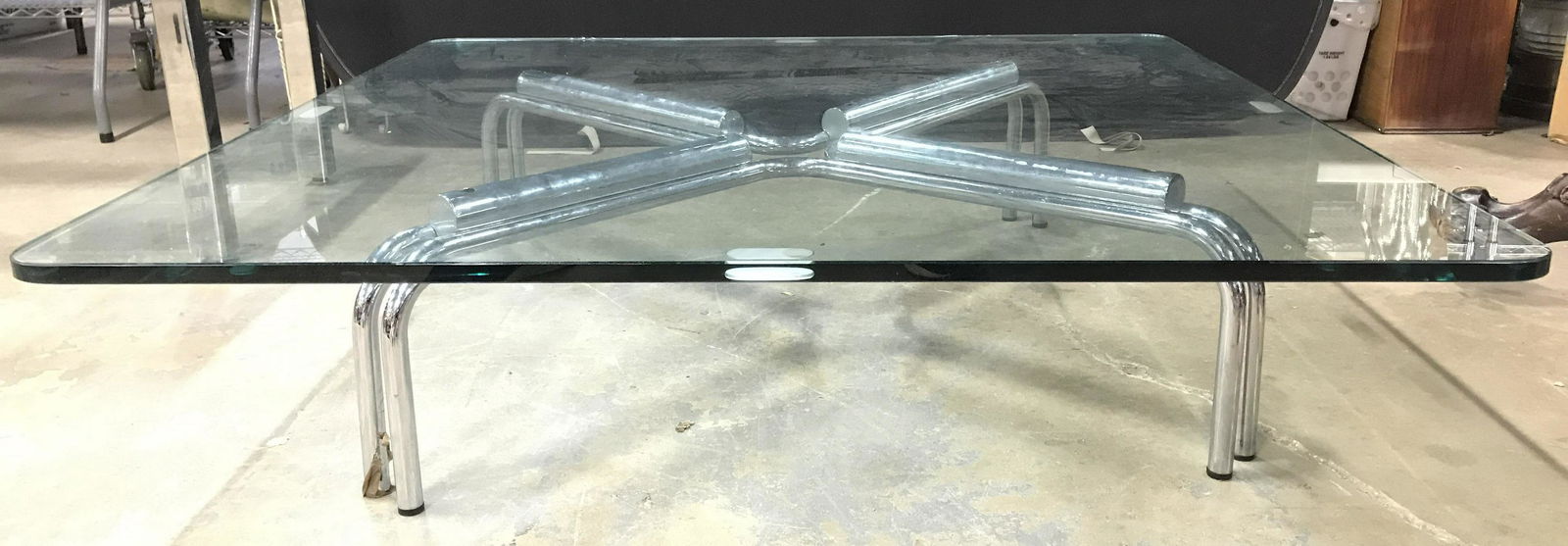 Low Profile Glass Top Coffee Table: Coffee table has silver toned metal legs and glass top. Legs appear to possibly be chrome. Tabletop has rounded edges. Table has low profile. Coffee table, glass top table, glass top coffee table, low