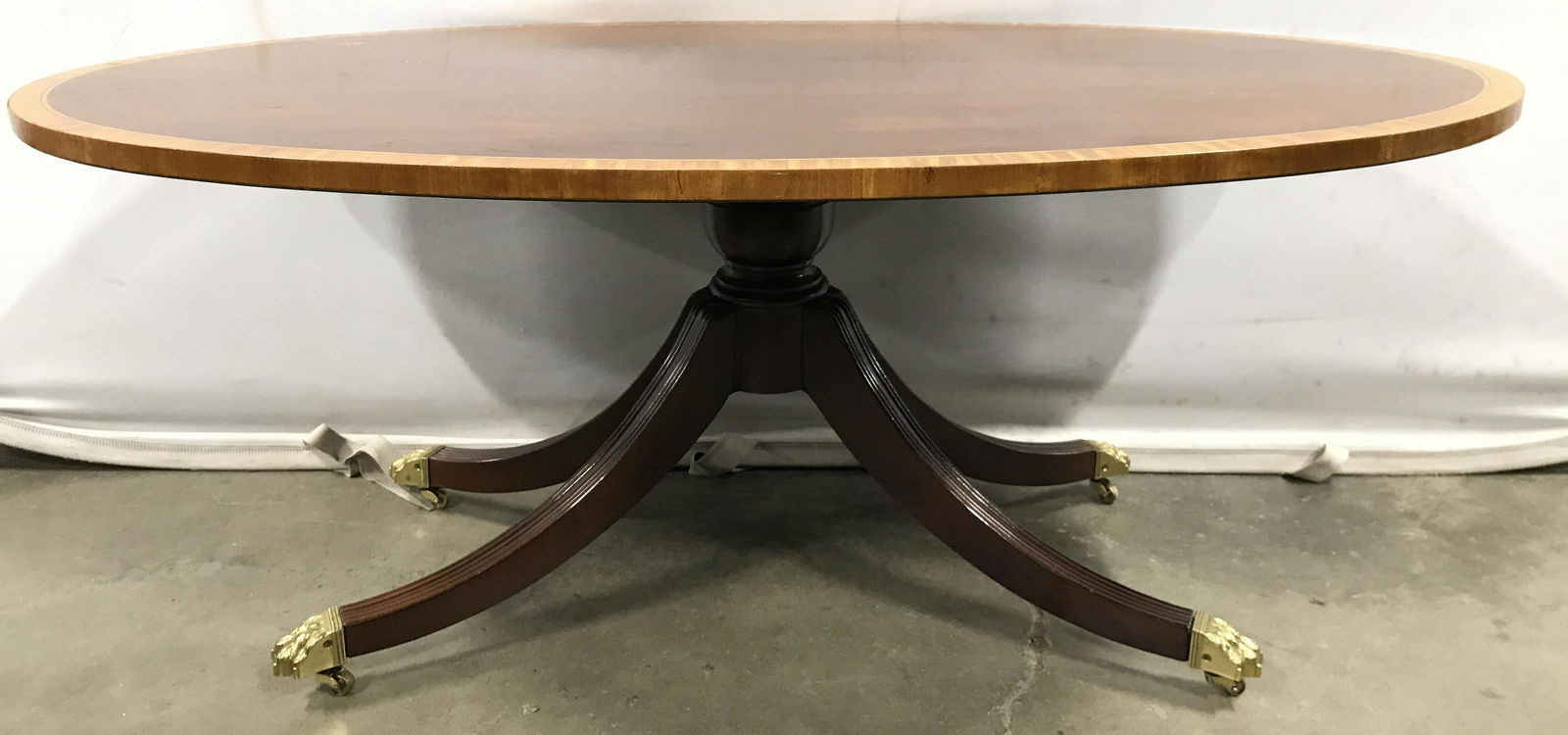 Oval English Style Wooden Coffee Table On Casters: Coffee table is wooden. Piece is oval shaped. Table has English style. Table is pedestaled. Table sits on gold toned casters with paw feet Piece measures approximately 44 inches long 18 inches tall 27