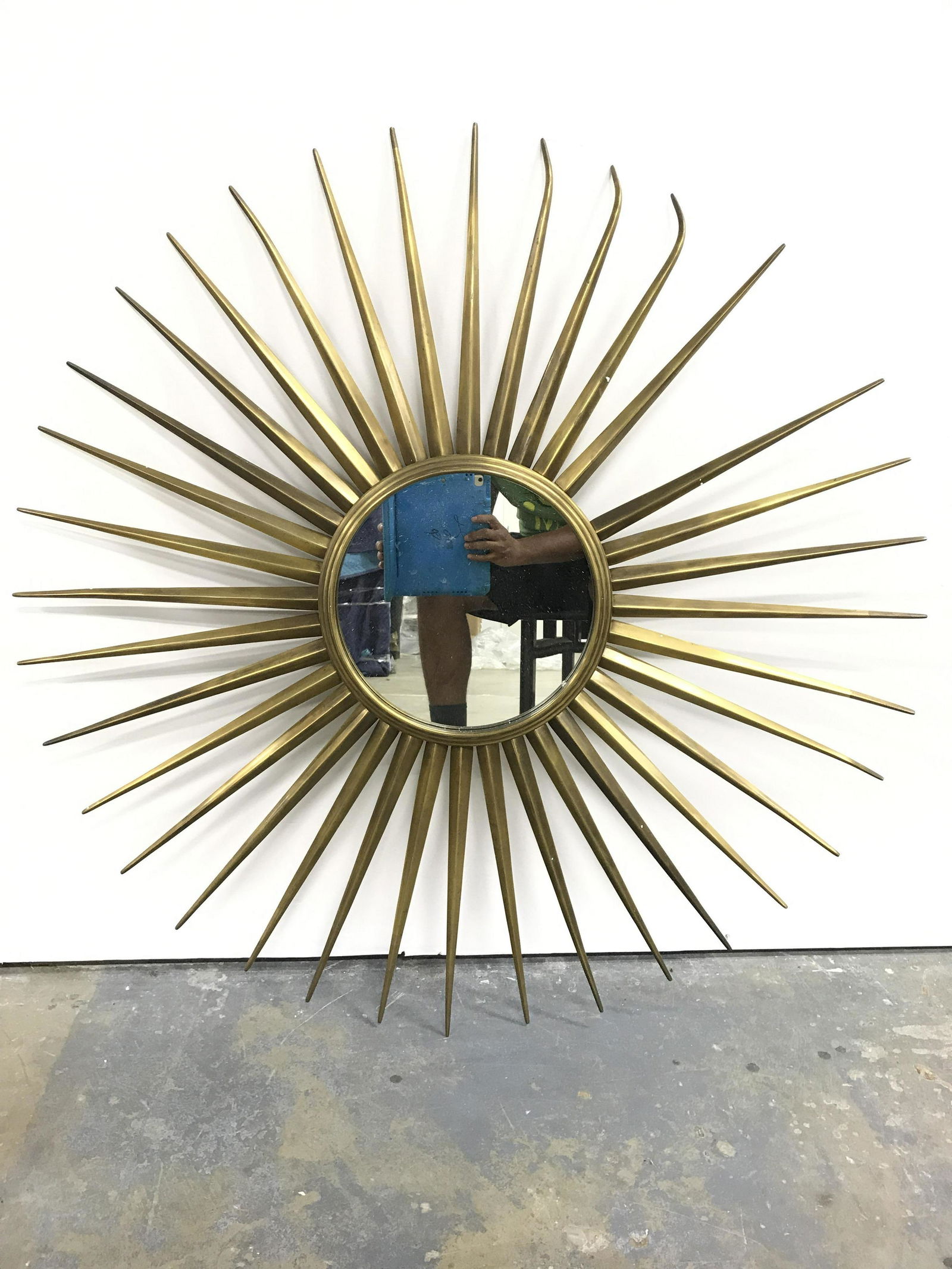 Gold Toned Brass Frame Sunburst Mirror: Mirror has gold toned brass frame with multiple spoke structures. Piece has circular mirrored surface. Mirror has sunburst frame. Piece is significantly weighted. Mirror, wall mirror, sunburst mirror,