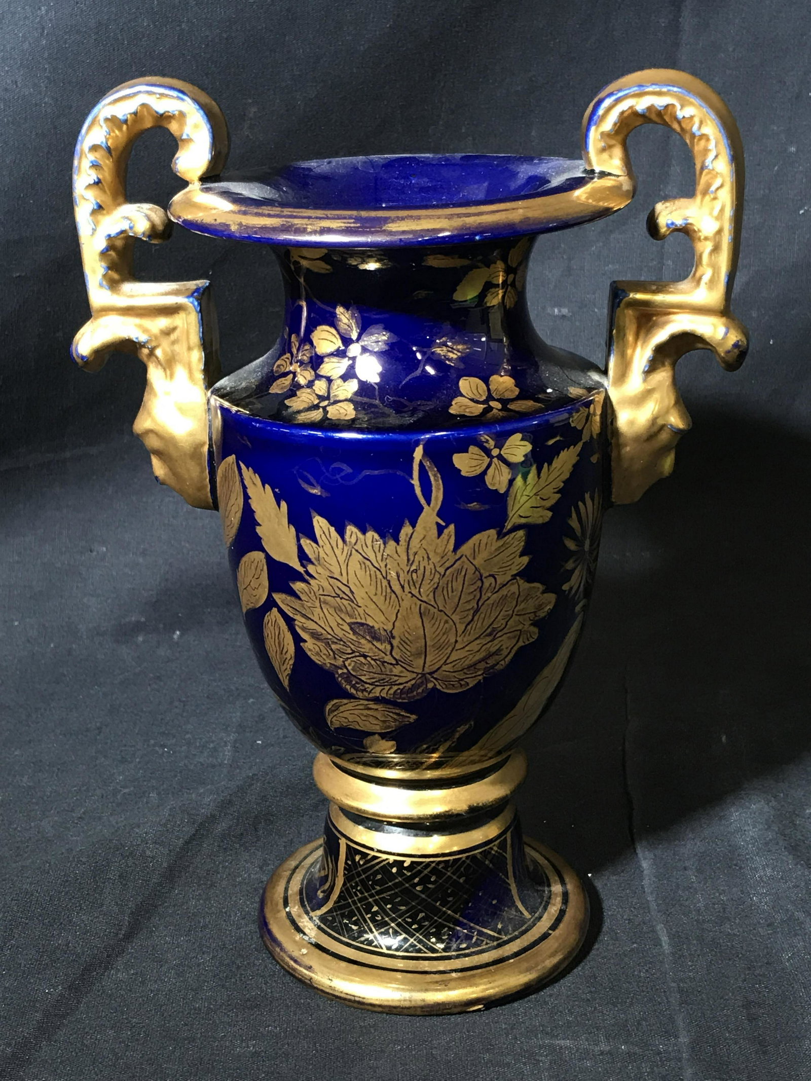 Porcelain Cobalt Blue Amphora Jug Vase: Porcelain Cobalt blue amphora, glazed in a cobalt blue color, no apparent stamps or signatures, painted with a gold tnd paint on the handles rim and base as well as vegetal designs to the front, measu