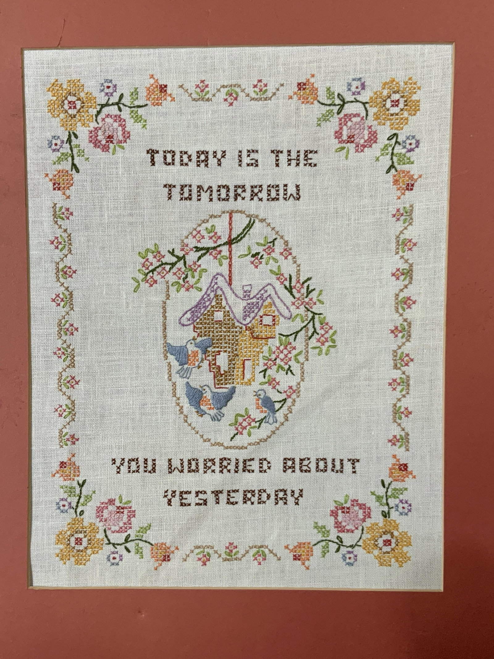 Cross Stitch Wall Hanging: Cross stitch wall hanging with flowers, birds, a tree house and age old adage that reads Today is the Tomorrow You Worried About Yesterday, the florals around the texts are in pinks oranges and yellow