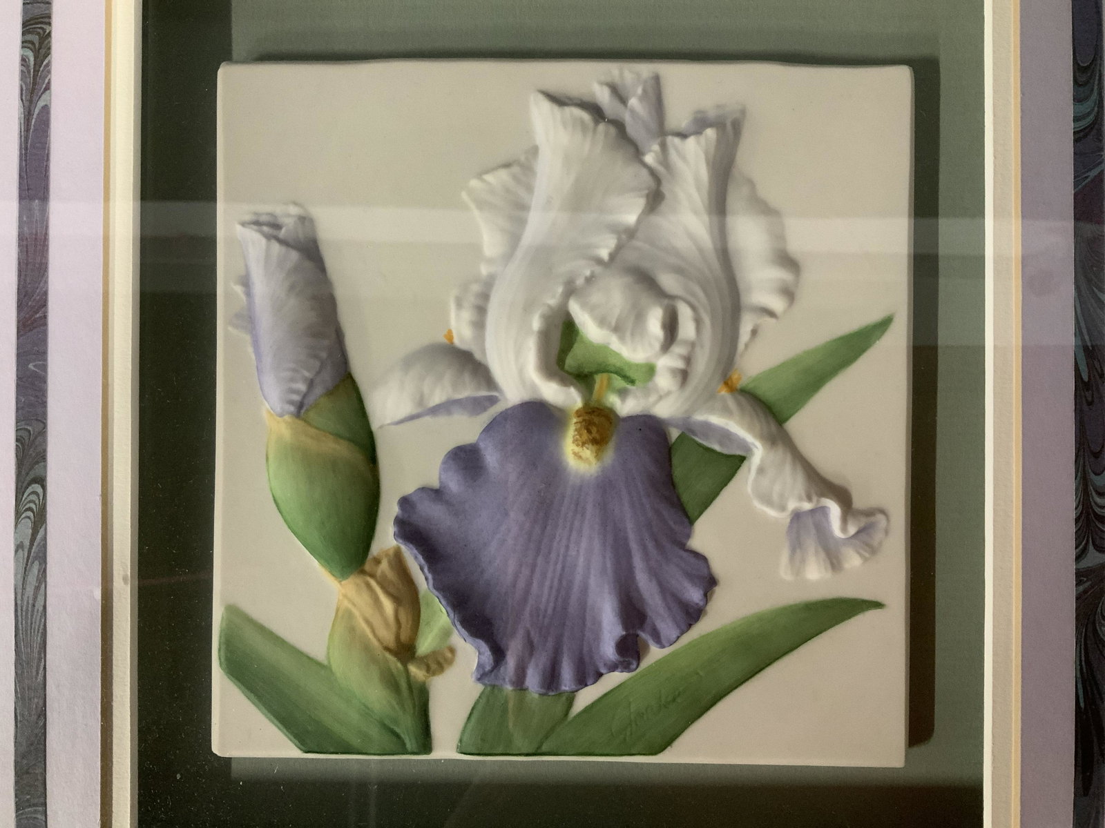 Ron Goeke Signed Bas Relief Porcelain Tile: Ron Goeke signed bas relief porcelain tile, signature carved in lower right of tile, a purple and white iris, Frame 14 3/4 in square. Tile 6 in square. wooden frame painted gold with some minor scratc