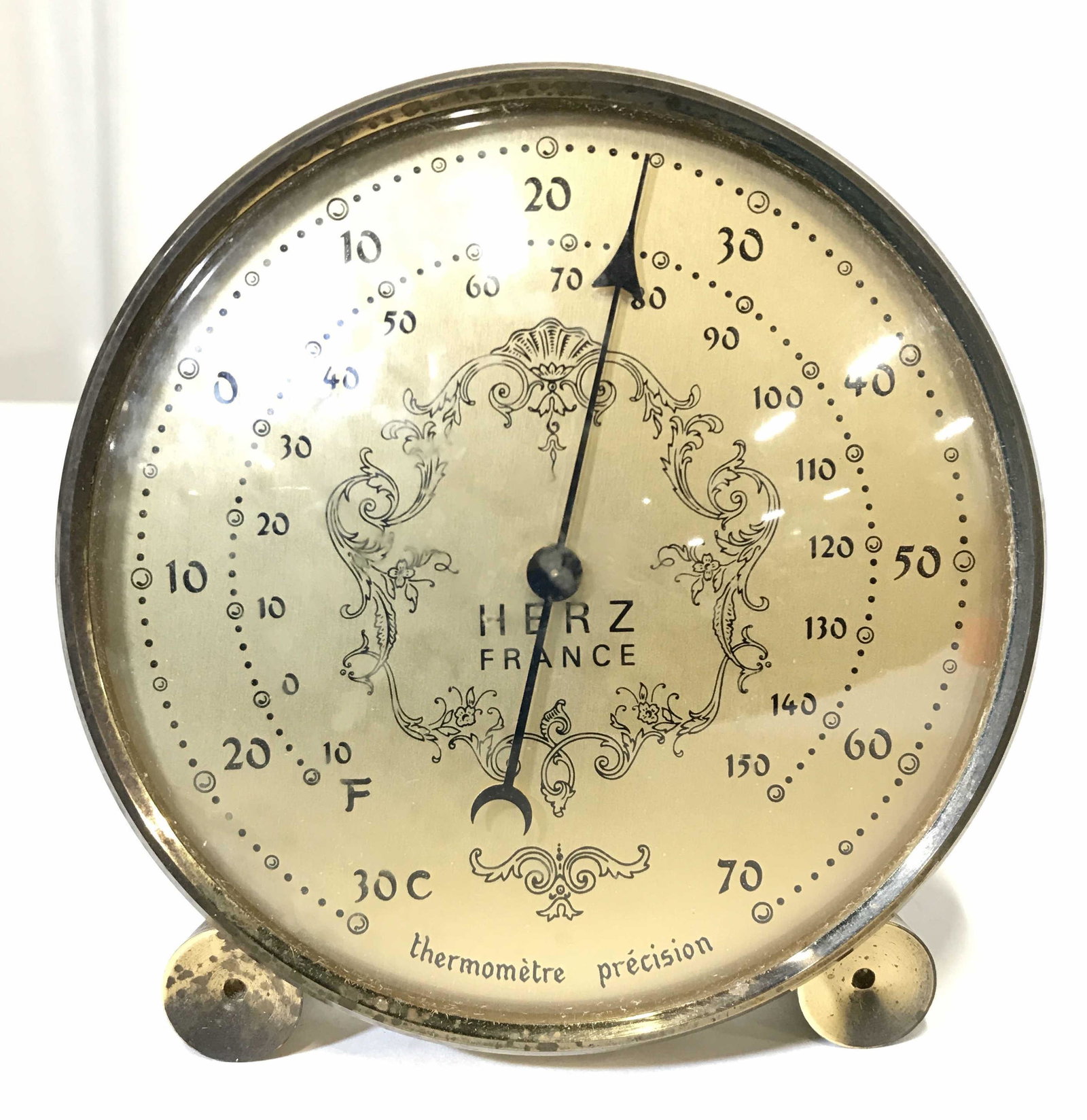 Vintage HERZ FRANCE Tabletop Thermometer: Thermometer face reads HERZ FRANCE THERMOMETRE PRECISION. Piece is gold toned possibly brass. Piece contains ornate detail near center. Thermometer reads in Celsius & Fahrenheit. Piece measures approx