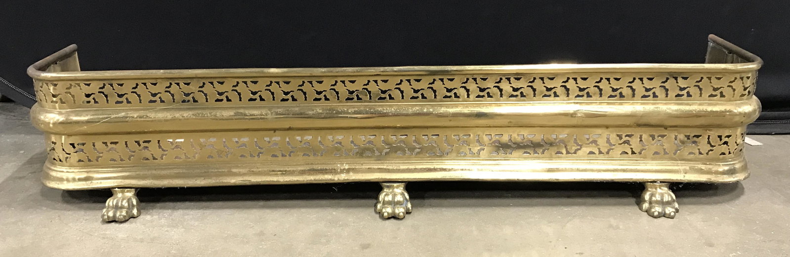 Vintage Brass Fireplace Fender: Vintage, possibly antique, fireplace fender. Fender is crafted from brass, three lions paws act as feet, and a perforated design decorates the fender. Measures approx 8.5 inches H, 47 inches W, and 14