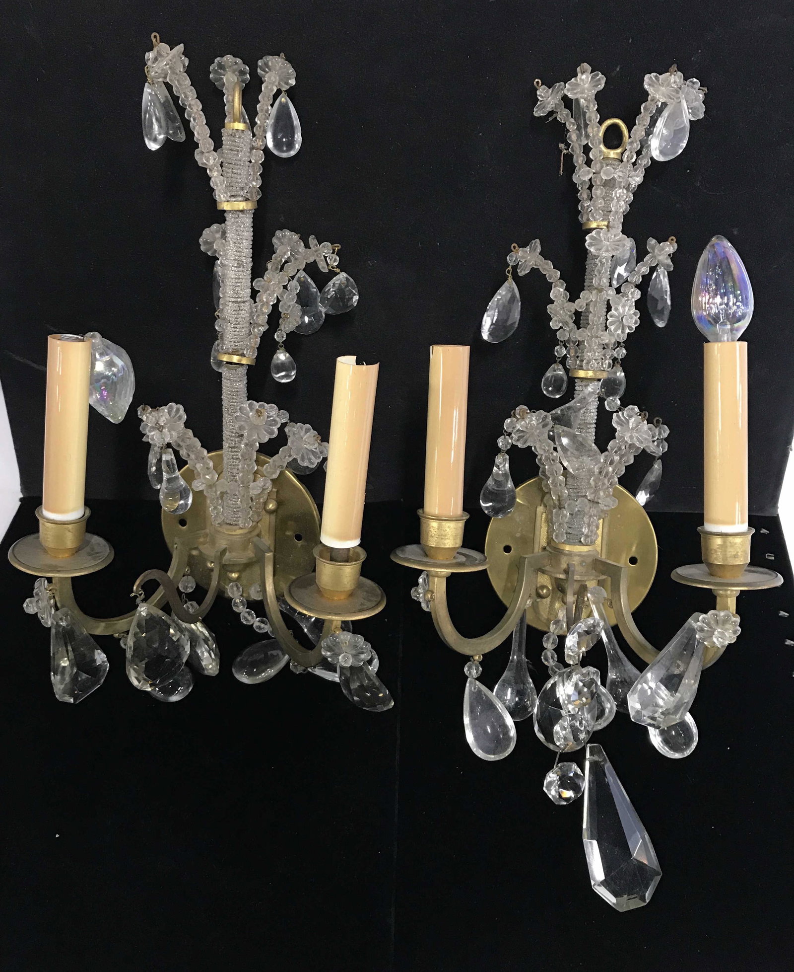 Pair Gold Toned 2 Arm Brass W Crystal Wall Sconces: Wall sconces are gold toned and appear to be brass. Measures approximately 18 inches tall 9 inches wide 5 inches deep. Each piece has 2 arms & multiple Cut glass prisms, home lighting, wall furnishing