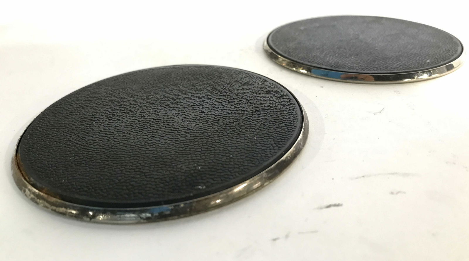 Pair Silver Toned Coasters: Coasters appear to possibly be black toned leather on top. Rest of coaster is silver toned & Metal, possibly sterling. Each measures approximately 3.5 inches wide. Coasters, bar accessories, Barware,