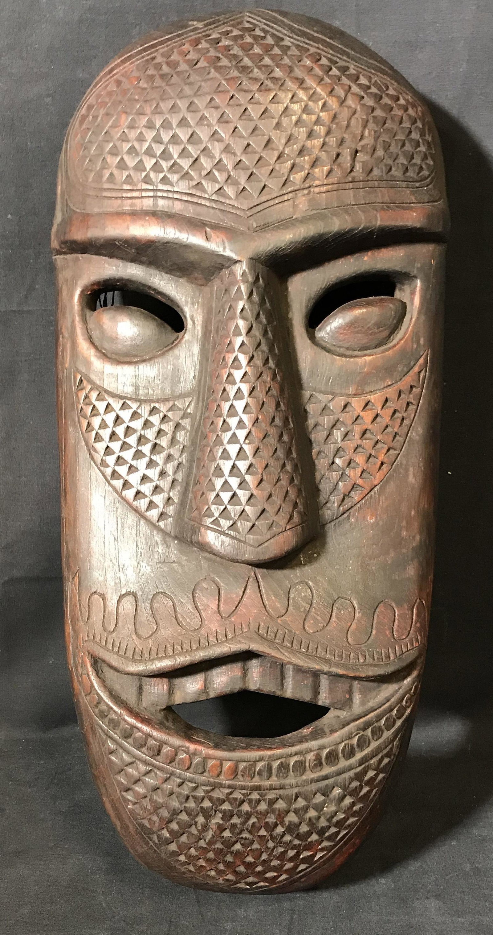 Far East Asian Hand Carved Wooden Mask: Far East Asian Hand carved wooden mask, possibly Indonesian in origin, mask depicts an elongated face with a highly textured surface, hanging wire and screws have been applied to the inside, wood stai