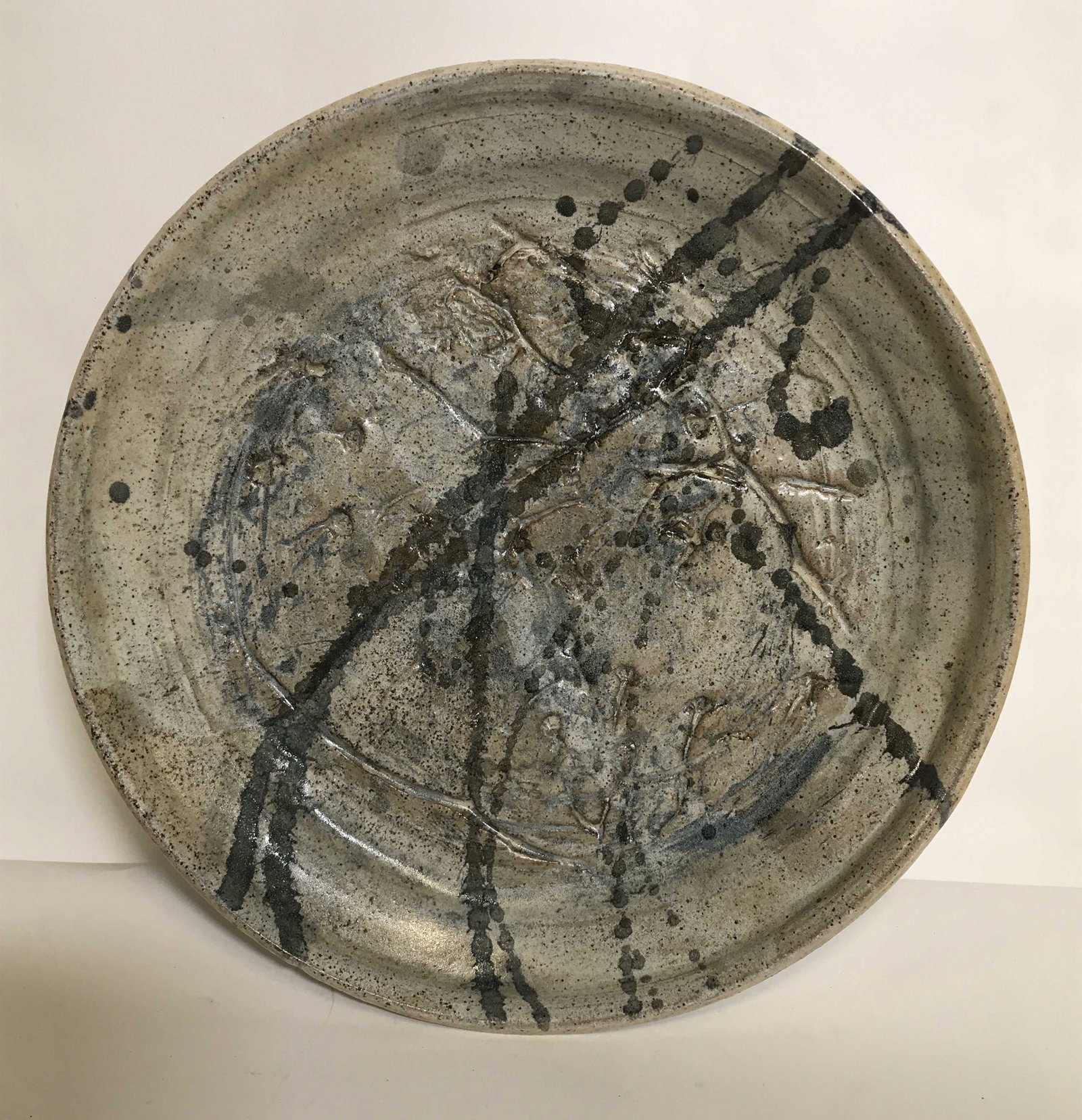 Vintage Art Pottery Incised Glazed Charger Dish: A vintage modernist abstract style art pottery plate with an all over speckled background with an incised decoration and a splatter design. The piece is in muted tones. It does not exhibit any damage.