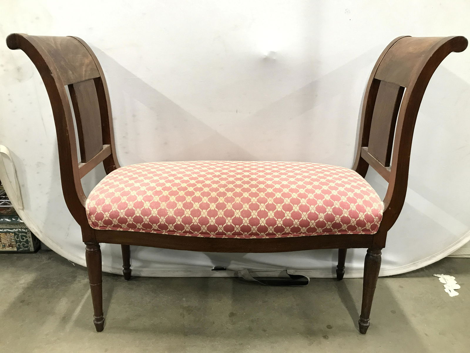 Vintage Upholstered Rolled Arm Entryway Bench: Bench has upholstered seat with coral & cream toned pattern detail. Piece has wooden arms with curved structures and rolled Tops. Edge of upholstery has double welting. Piece also has carved wooden le