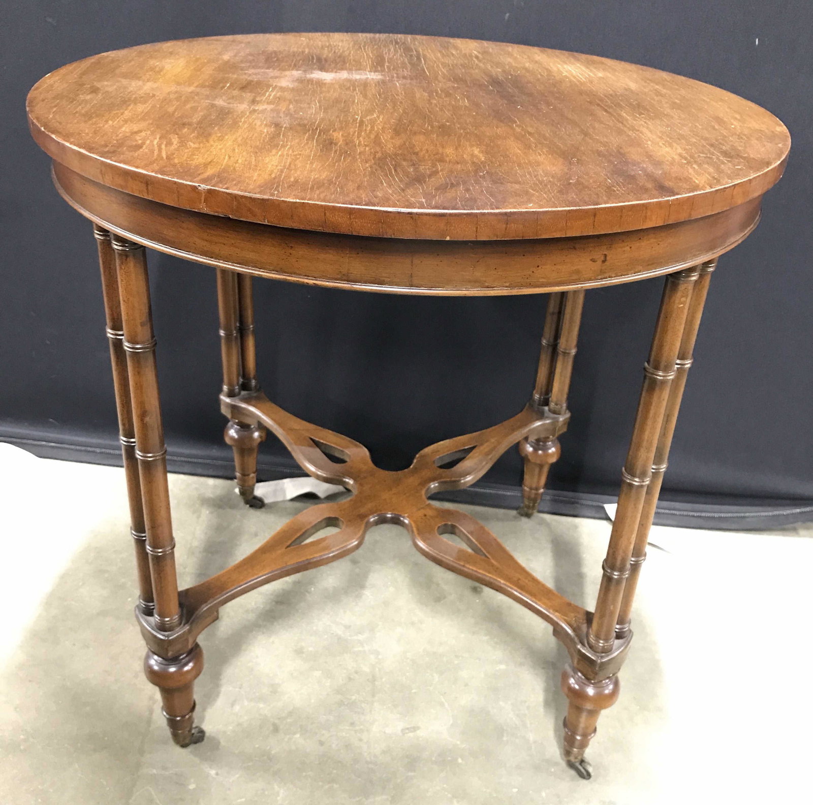 Vintage Round Wooden Side Table On Casters: Side table is vintage and wooden. Piece has carved detail resembling bamboo in some areas. Legs have stretchers in between legs. Side table is round in shape. Piece measures approximately 28 inches ta