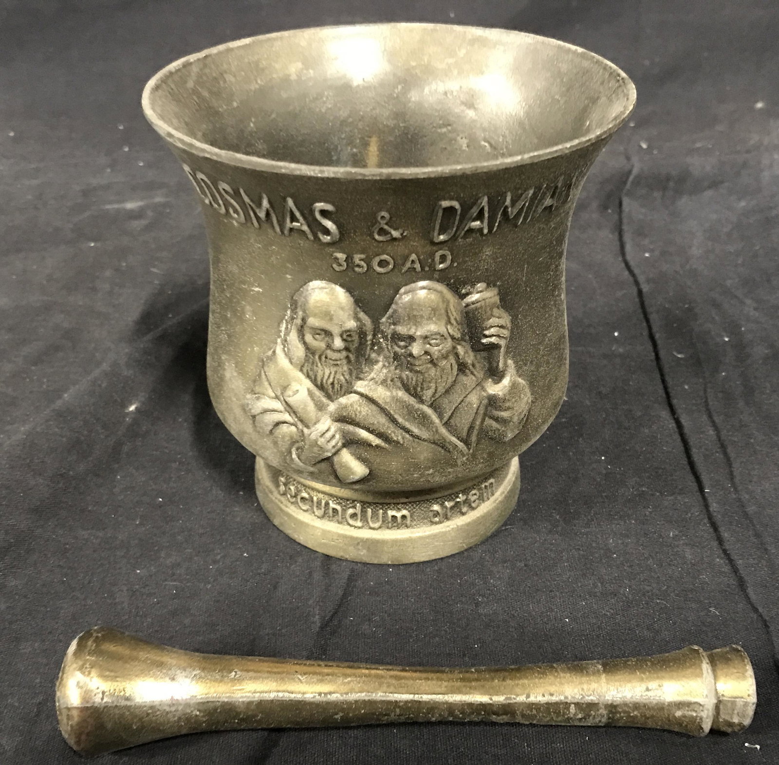 Cosmas & Damian Bronze tnd Metal Mortar and Pestle: Bronze Mortar and Pestle, front of mortar displays two bearded men with scrolls and a cup, text to front reads ‘Cosmas & Damian’, Latin text to lower section reads ‘Secundum artem’ or ‘accor