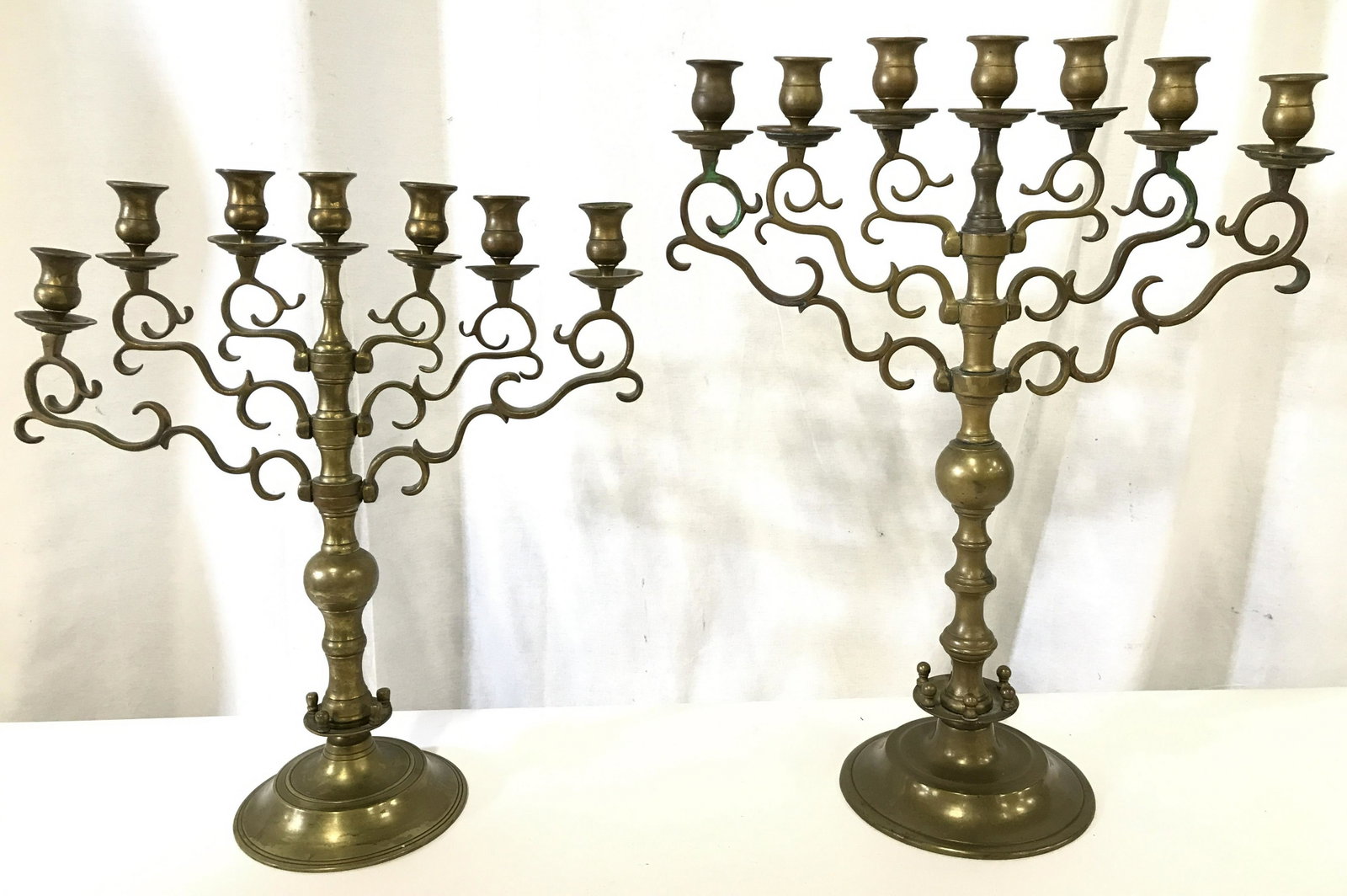 Lot 2 7 Arm Gold Toned Brass Candelabras: Candelabras are gold toned and brass. Each candelabra has 7 arms. Pieces have ornate c & S curve detail. Bases of each are round in shape. Largest candelabra measures approximately 21.5 inches tall 16