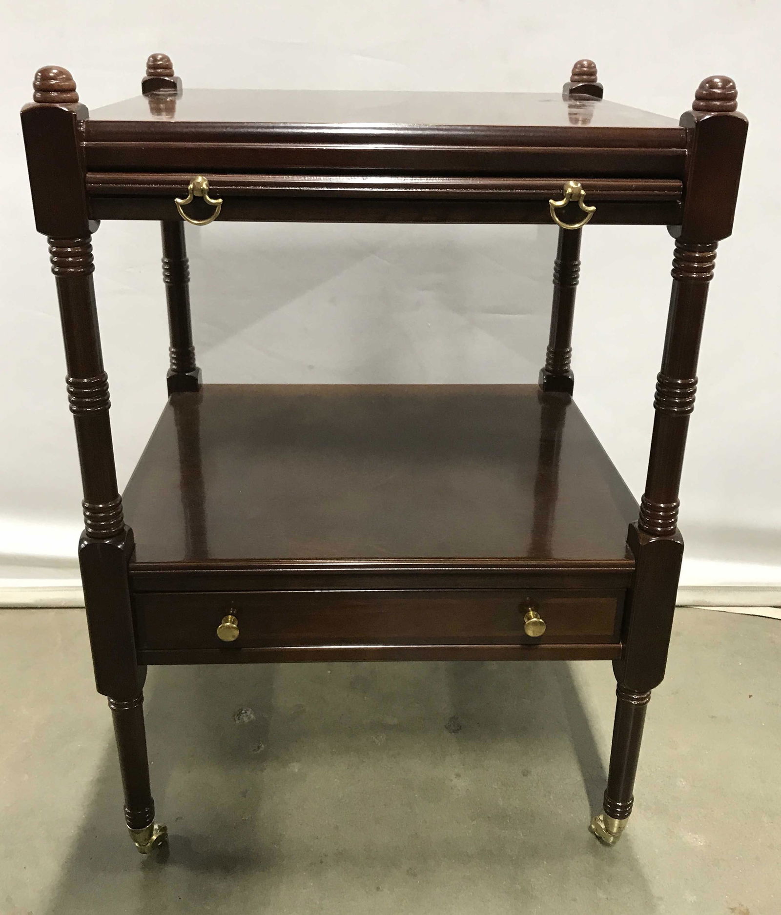 THE BOMBAY COMPANY Tray Side Table On Castors: Side table with extending tray, one drawer, drawer and tray pulls are brass, each leg sits on a brass castor. Label on underside reads as THE BOMBAY COMPANY. Measures approx 25.5 inches H, 15.75 inche