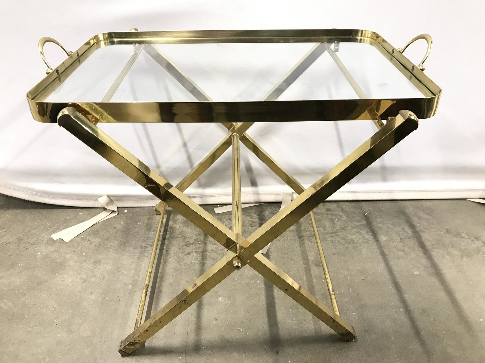 Brass Folding Tray Table With Butlers Tray Top: Tray table is gold toned and brass. Piece includes tray top with handles and glass surface. Base of table folds. Piece when set up measures approximately 22 inches long 20 inches tall 17 inches deep. 