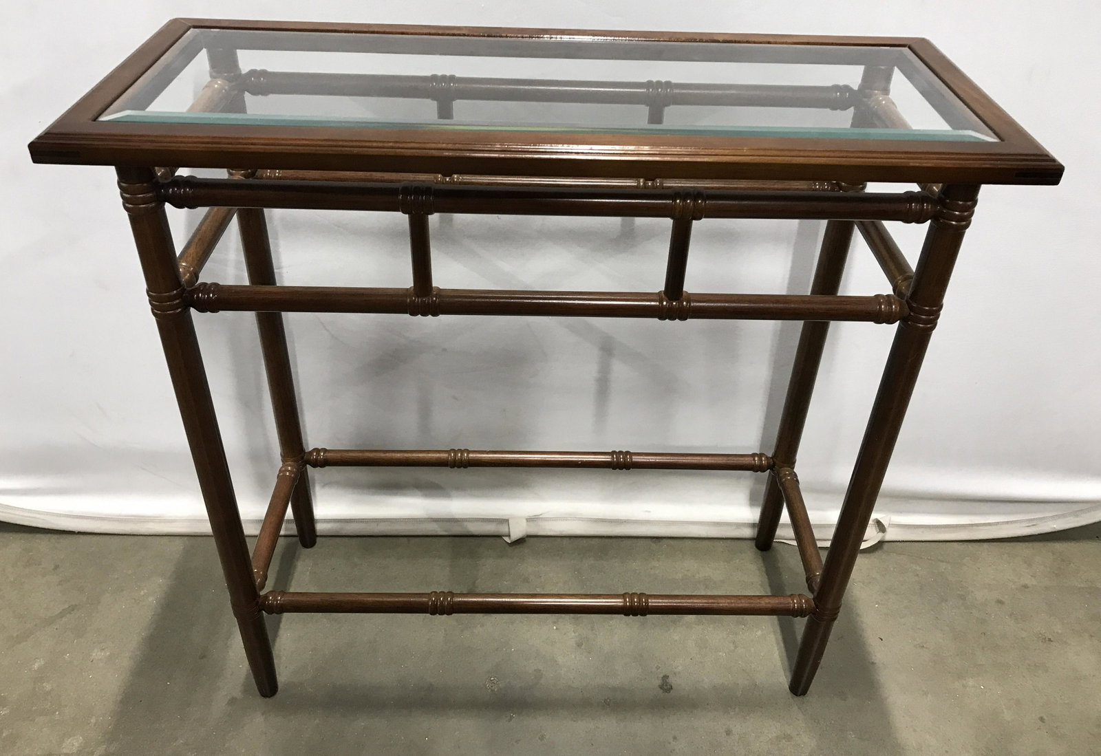 THE BOMBAY COMPANY Walnut Toned Side Table: Walnut toned side table. Table is glass topped, the label on underside reads as THE BOMBAY COMPANY. Measures approx 29.5 inches H, 31 inches W, and 12.25 Inches deep. Hall table, accent table, sofa ta