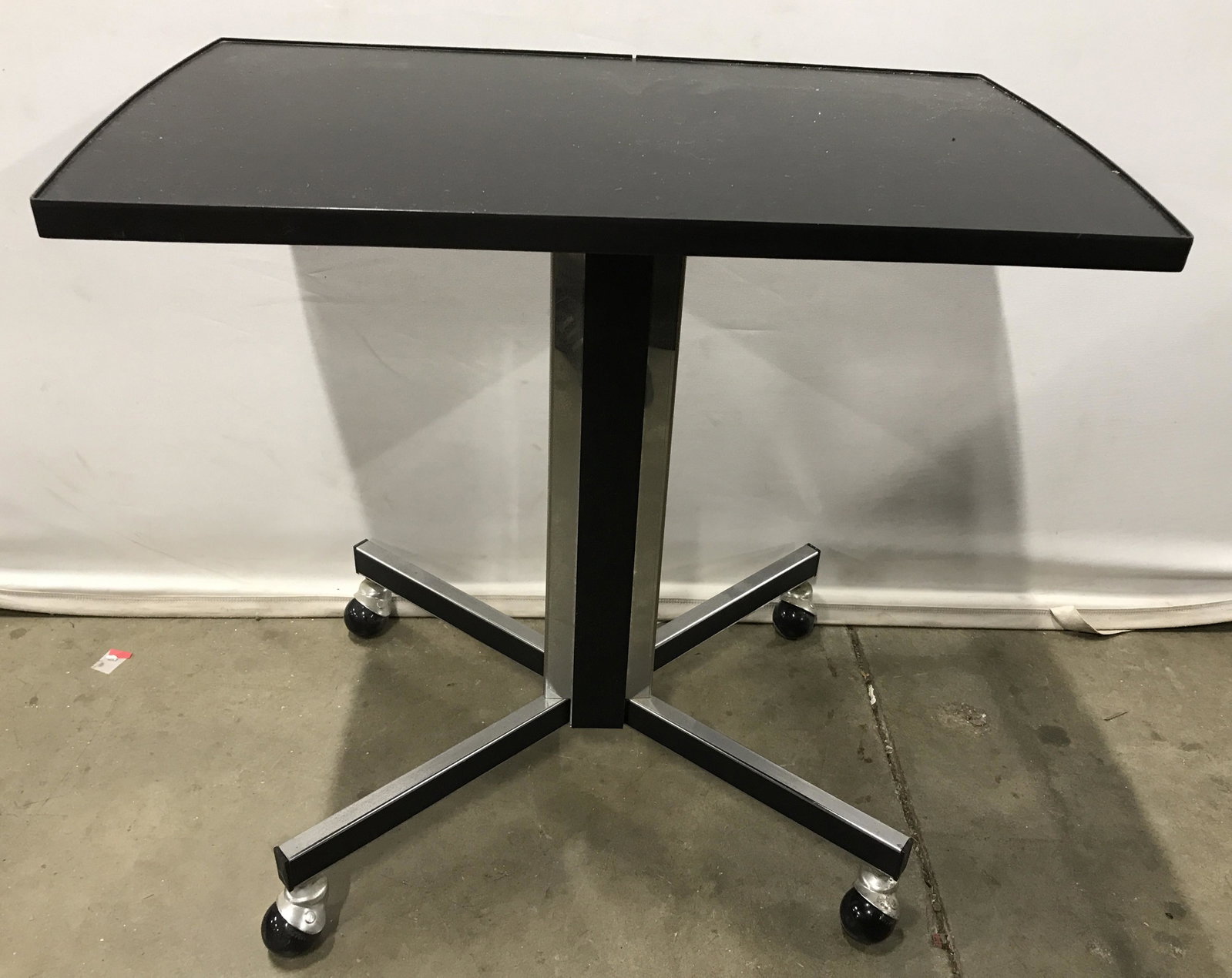 Vintage Wheeled Tray Table: Vintage tray table. Tray is colored black, supported by metal column, black strip runs down the center of the column. 4 orb shaped wheels. Measures approx 25.5 inches H, 27.25 inches W, 15.75 inches D