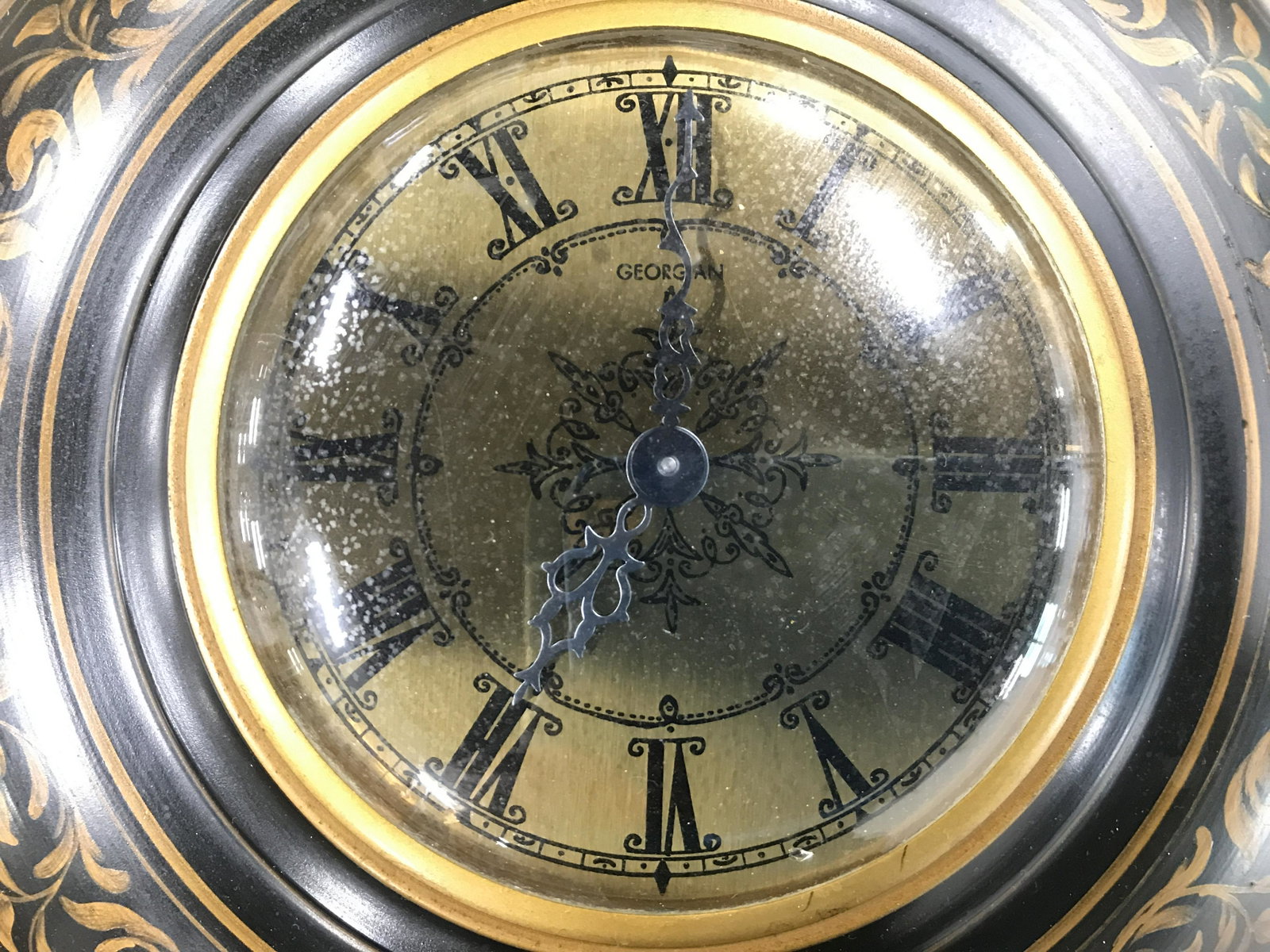 Vintage GEORGIAN Round Hanging Metal Wall Clock: Clock appears to be vintage. Piece is black with gold toned ornately painted detail. Piece has gold toned Clockface with black toned Roman numeral detail. Piece has hanging loop at top. Clock face rea