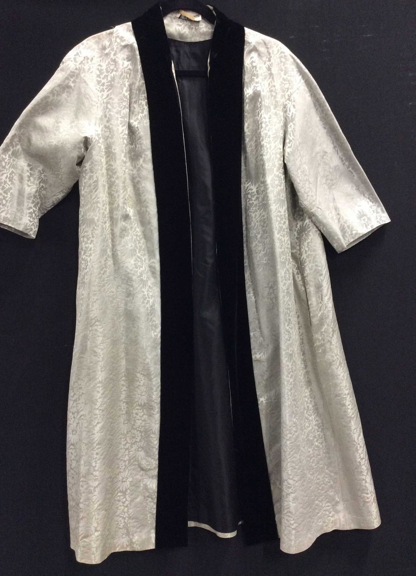 Vintage Lilli DIAMOND Brocade House Coat: Metallic Silver Brocade with tonal florals, Shawl Collar down Center is black velvet, interior lined, Mid weight fabric, side pockets. Designer label reads ORIGINAL LILLI DIAMOND OF CALIFORNIA. 42.5 i