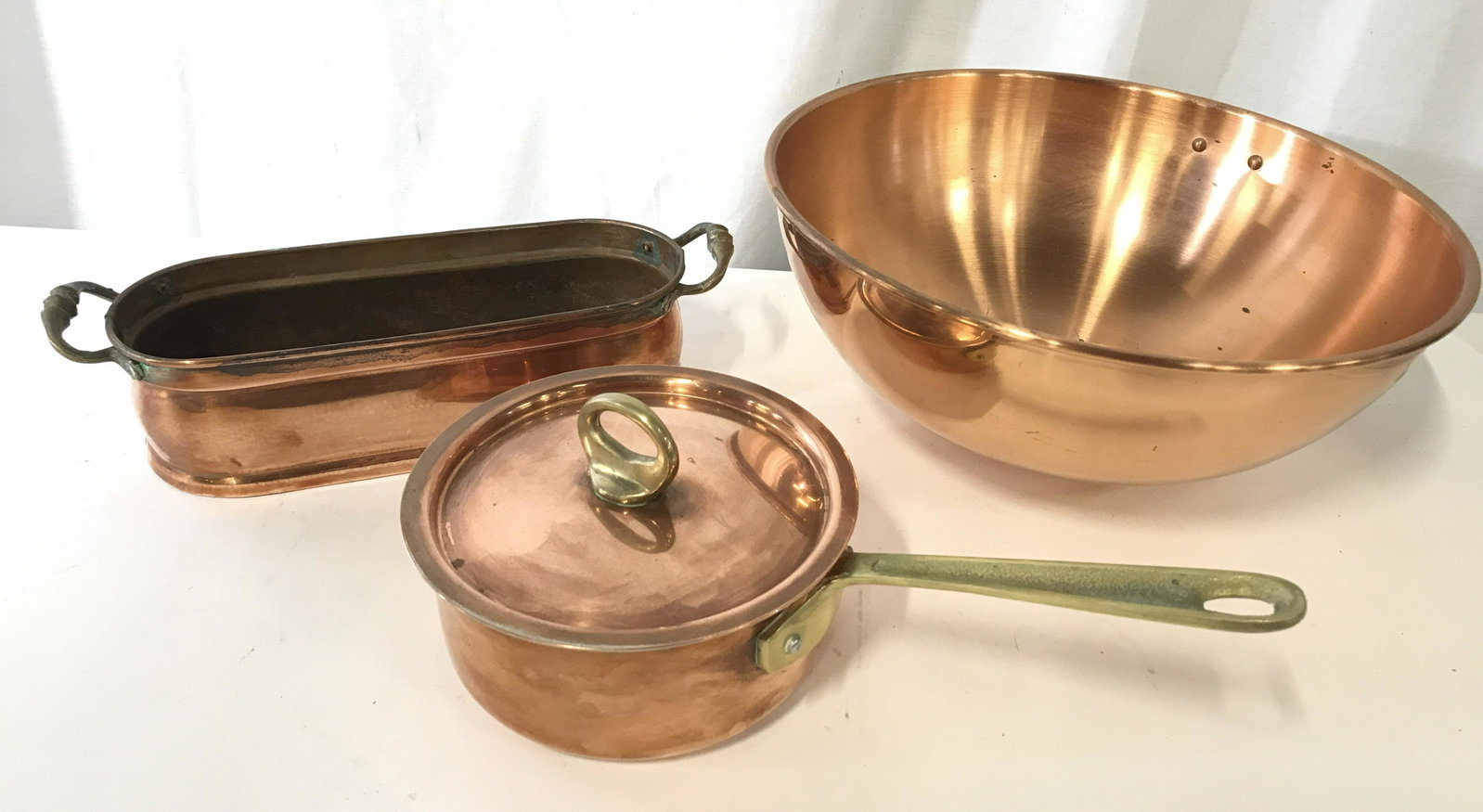 Lot 3 Copper Kitchenware, Accessories: Copper cooking accessories. Includes a bowl, a pot, and a bread pan. The largest piece measures 5 inches H, and 11.5 inches in diameter. Pot is brass handled, handle has a pitted texture. Bread pan ha