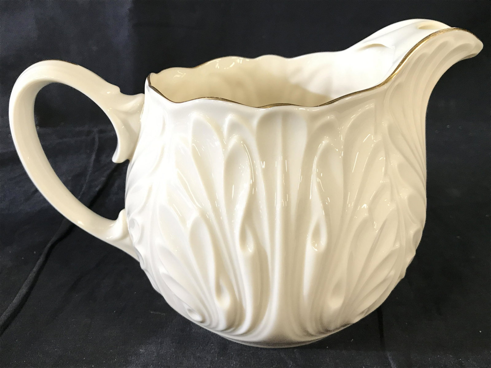 LENOX Porcelain Pitcher: Pitcher is marked LENOX on underside. Piece is cream toned with gold toned rim and accent on handle. Piece also has beveled relief detail. Piece measures approximately 9 inches long with spot and hand