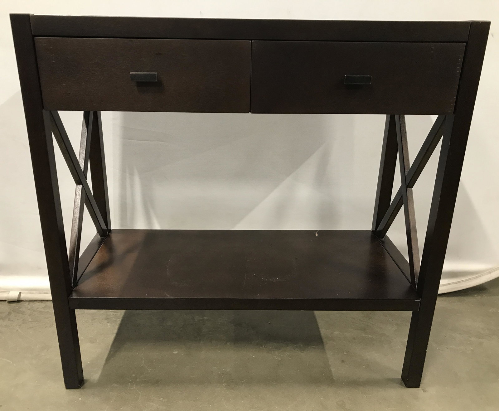 Brown Toned Wooden Console Table W Drawers: Console table is brown toned and wooden. Table is includes 2 drawers each with rectangular prism shaped handles. Legs have X Structure in between & low shelf area. Console table, wooden console table,