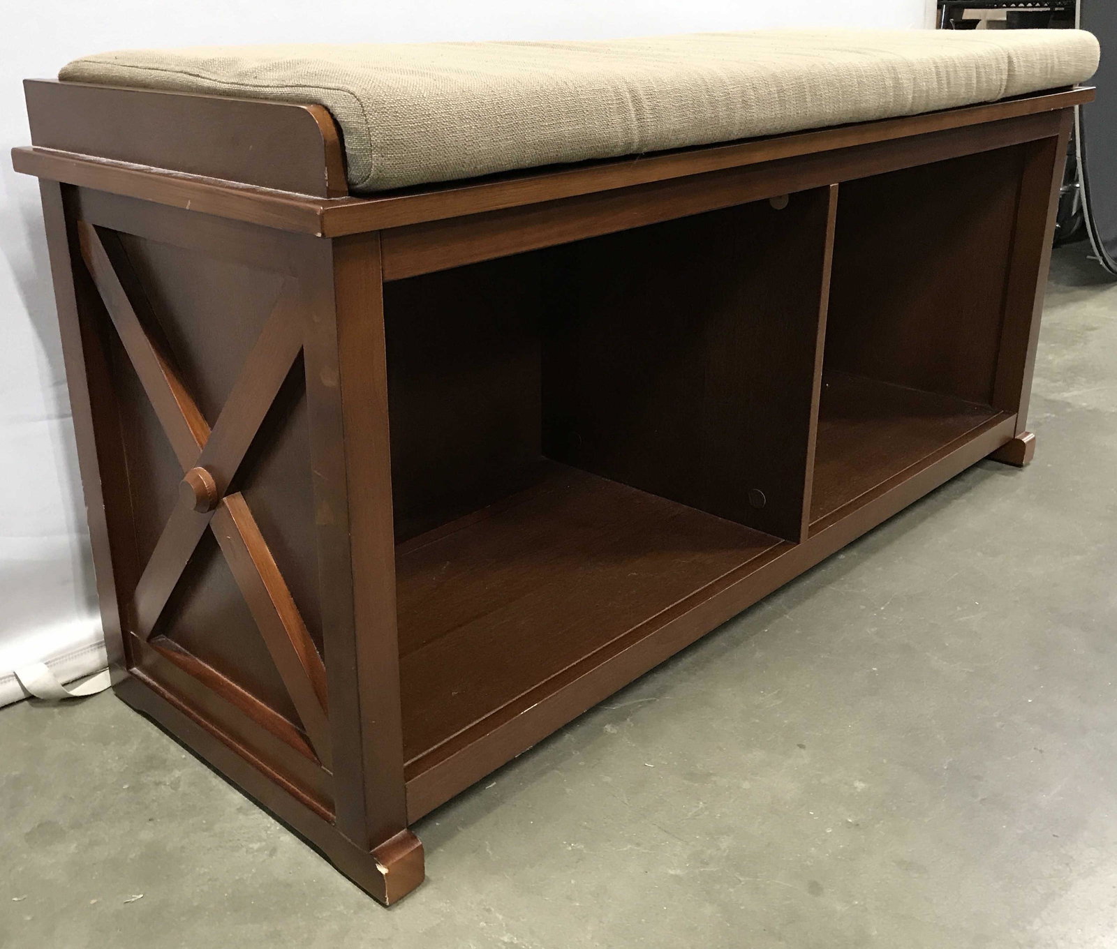 Vintage Wooden Shoe Storage Bench: Bench is wooden with a light brown beige tone. Top of bench has sand toned cushion. Storage area is divided into 2 areas. Each side has X shaped structure. Piece measures approximately 48 inches long 