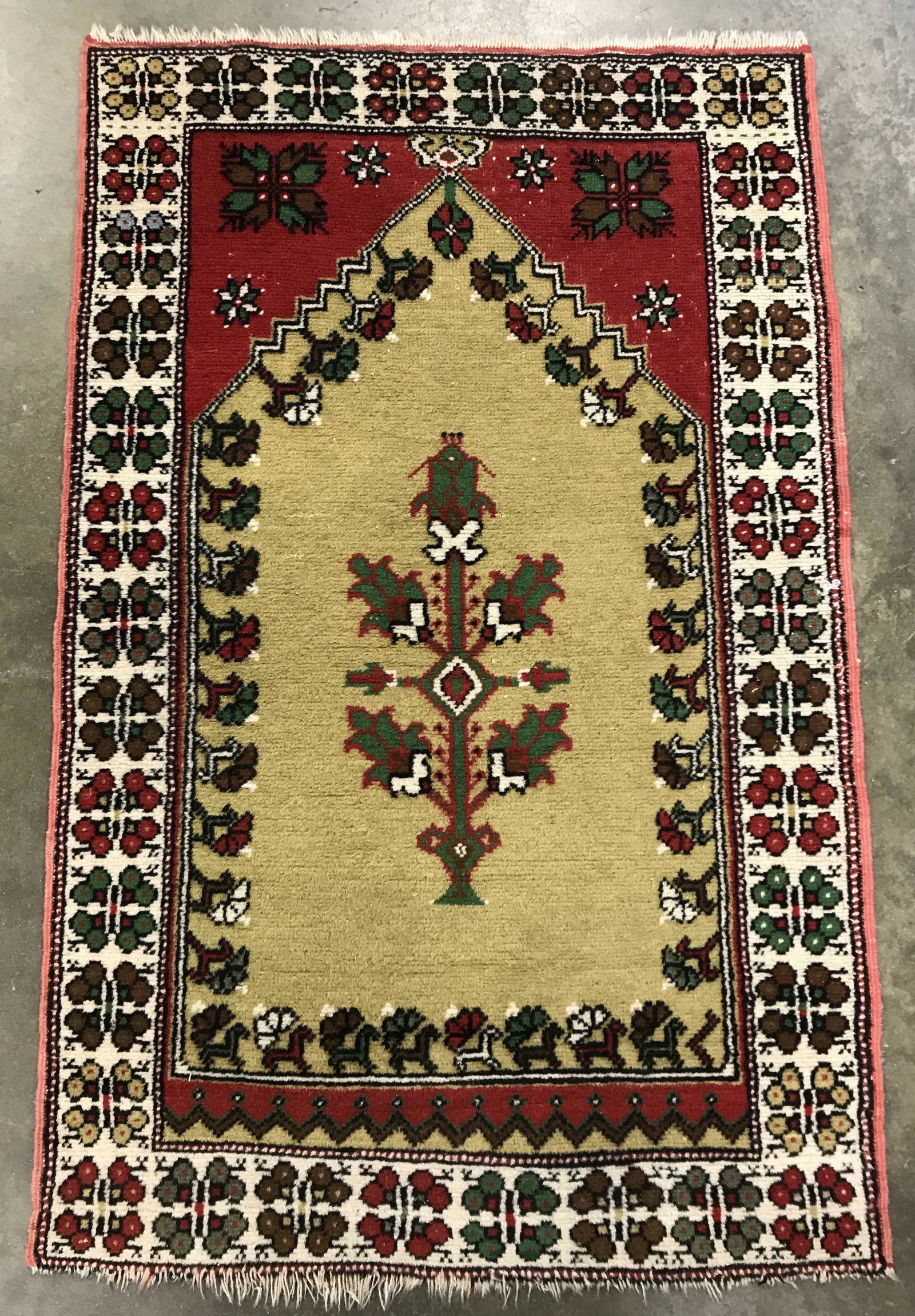 Vintage Wool Area Rug: Vintage European style rug. Depicts a floral pattern along its border, and a tree at its center. Measures approx 53 inches long, and 33.5 inches wide. Carpet is frilled. Wear is consistent with age an