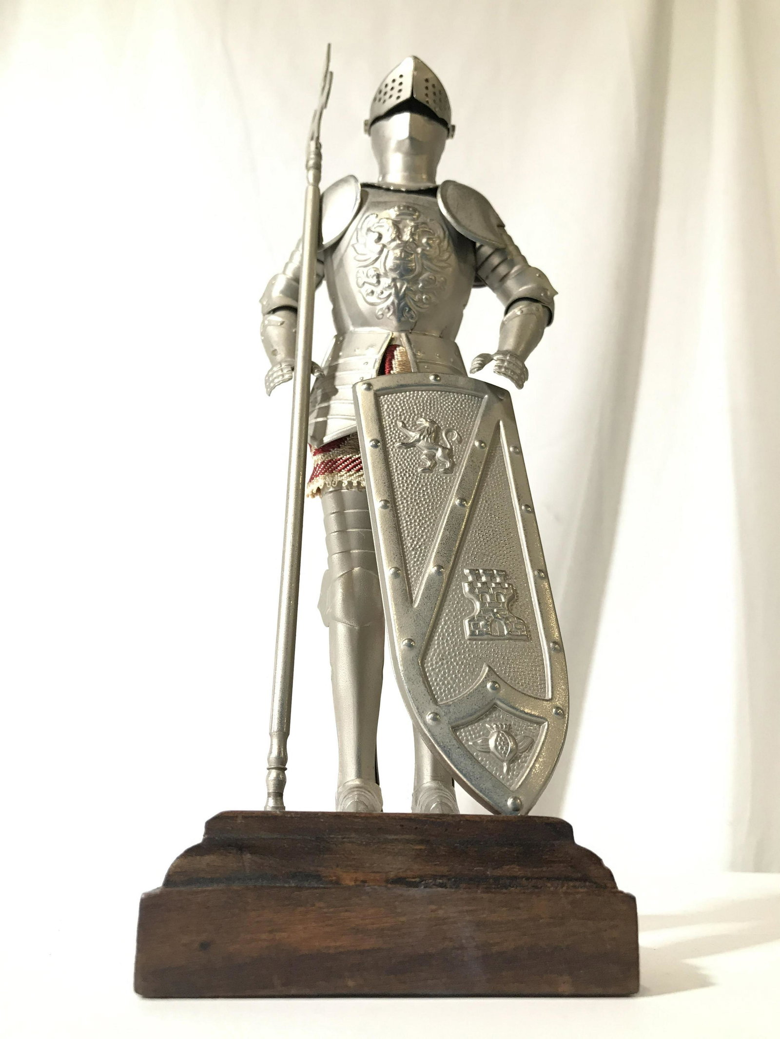 Vintage Metal Knight In Armor Figure W Wood Base: Knight figure is silver toned and metal. Piece has square shaped wooden base. Depicts an knight in armor holding and shield and weapon. Piece measures approximately 11 inches tall 3.5 inches wide and 